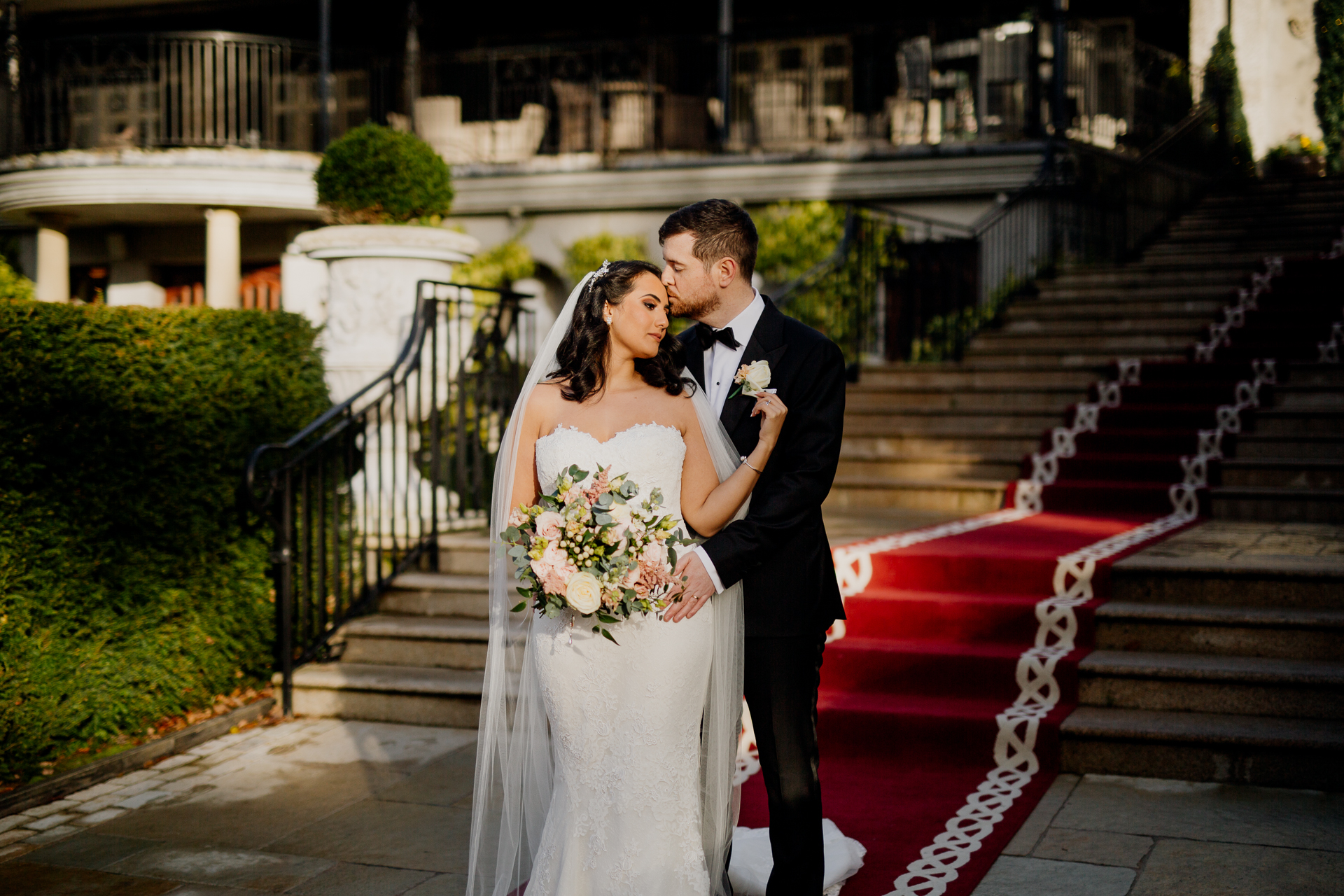 A newlywed couple kissing on the red carpet stairs of Cabra Castle during golden hour