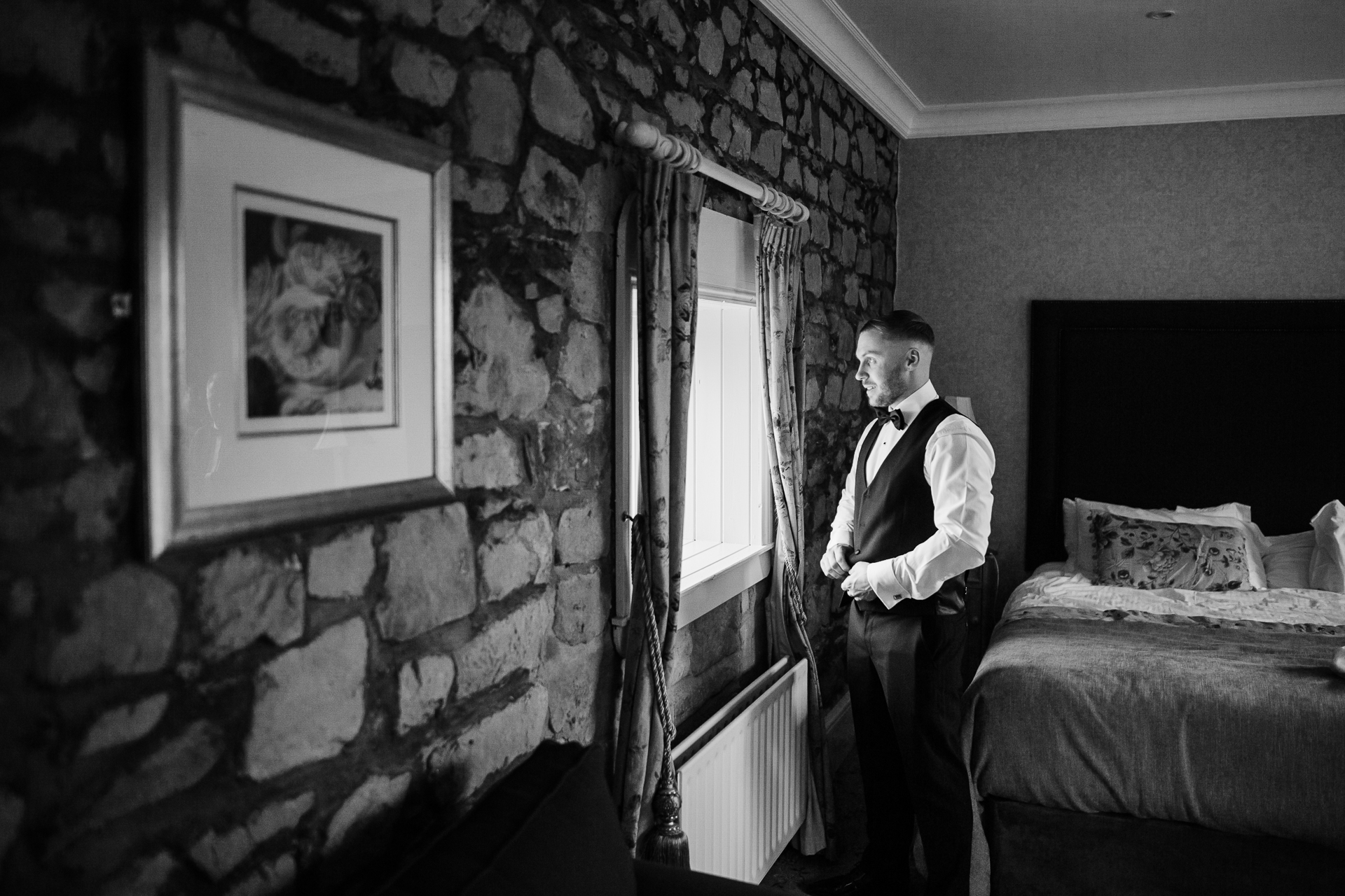 Groom standing by the window getting ready before Cabra Castle wedding in black and white