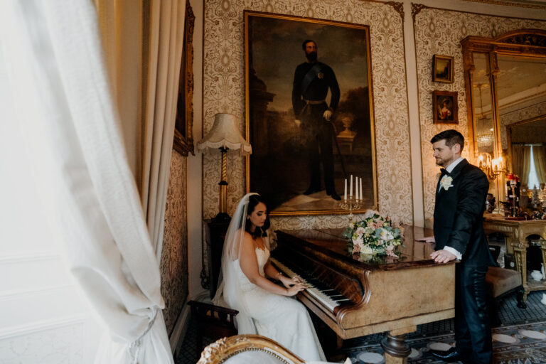 Bride plays a vintage piano at Cabra Castle as the groom watches — elegant moment inside the castle, captured by a Dublin Wedding Photographer.