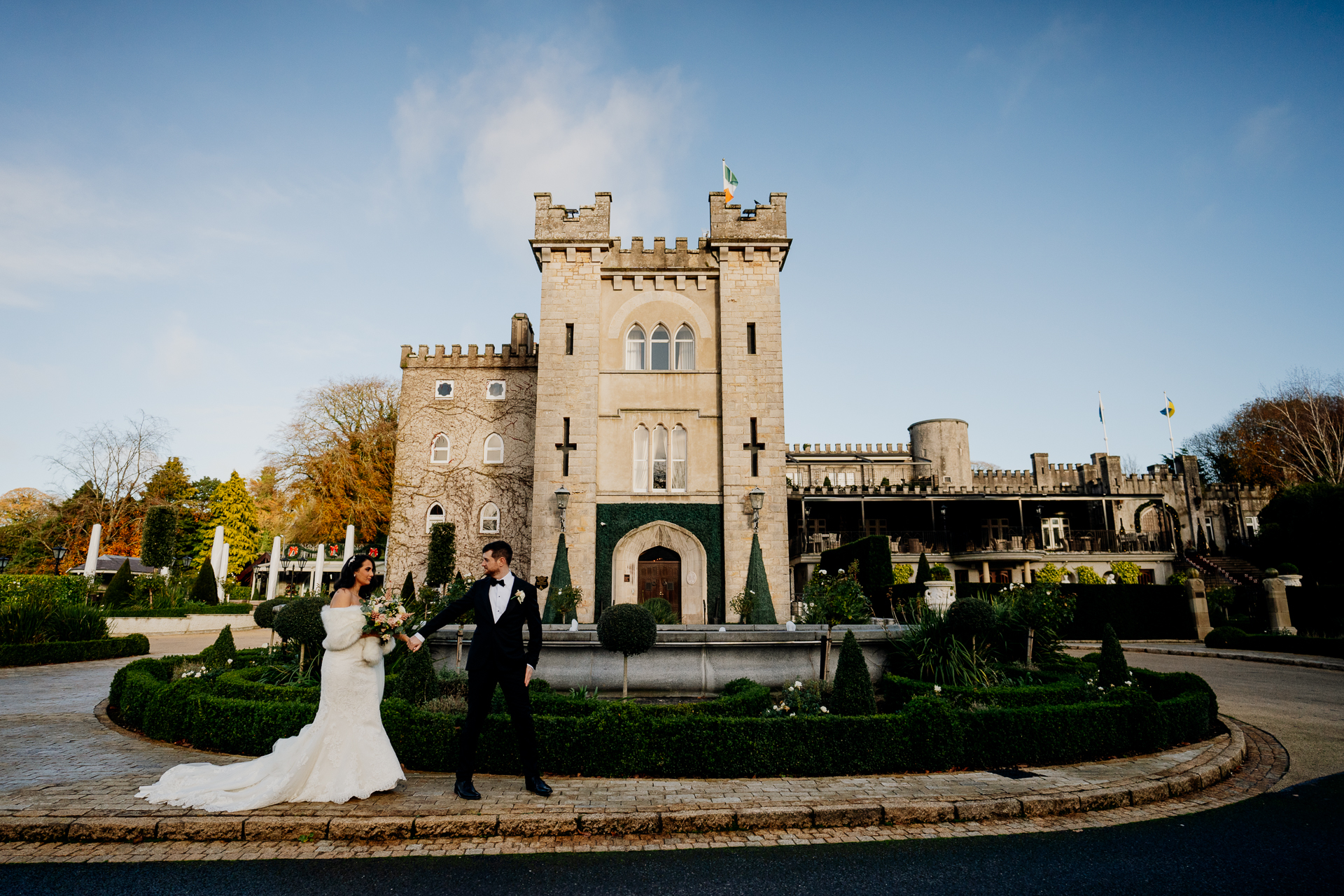 A bride and groom standing in front of the grand facade of Cabra Castle under a clear blue sky