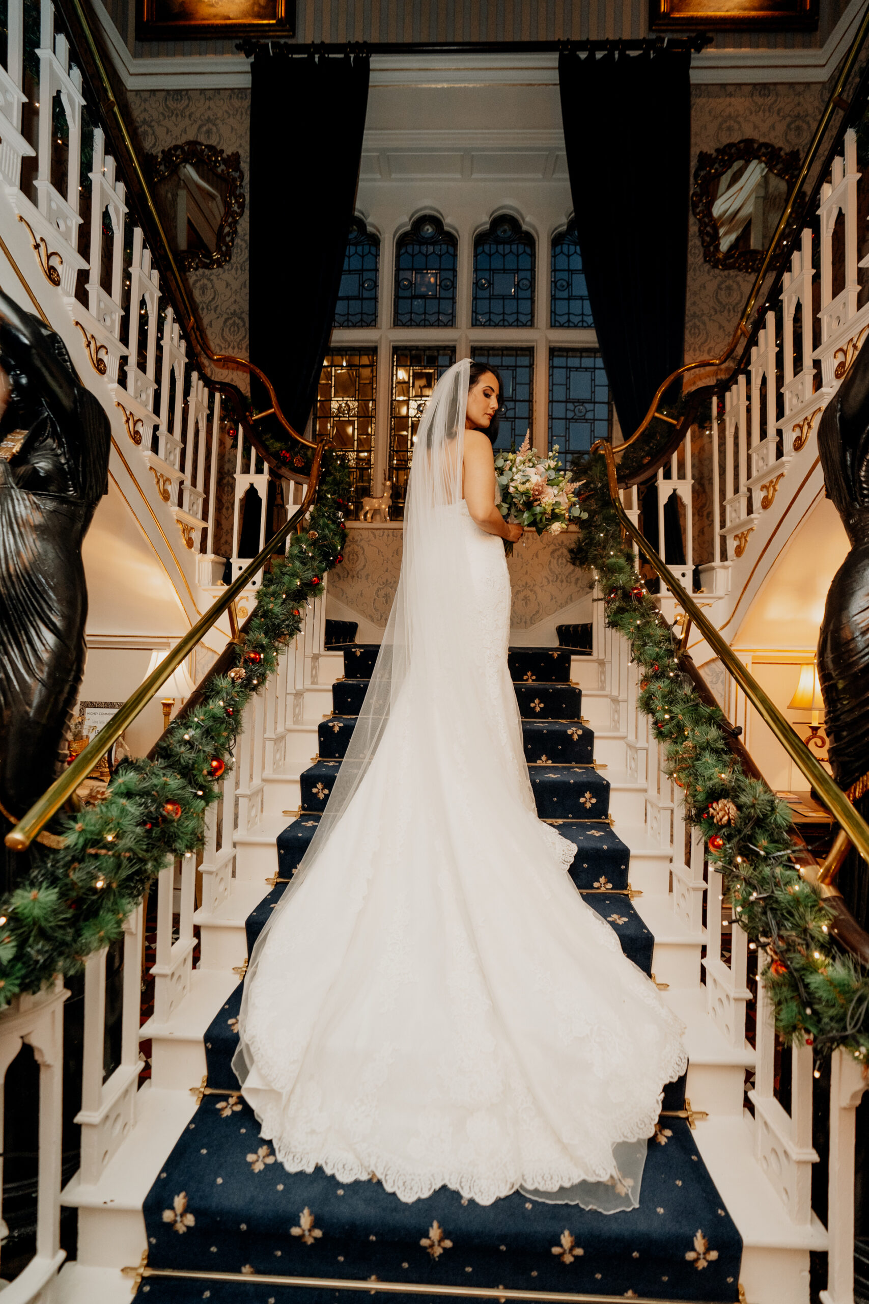 Bride standing at the top of the grand staircase inside Cabra Castle, her long train flowing behind her in a cinematic bridal portrait.