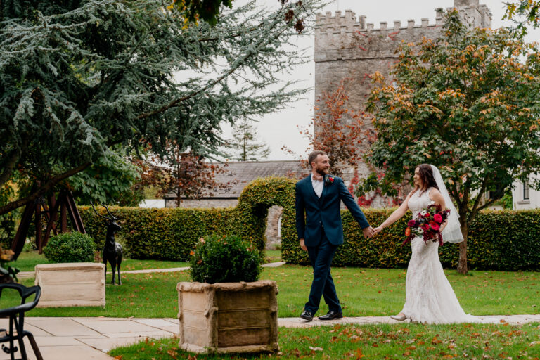 Bride and groom walking hand in hand through the gardens of Cabra Castle on their wedding day – captured by a Dublin Wedding Photographer in elegant, candid style.