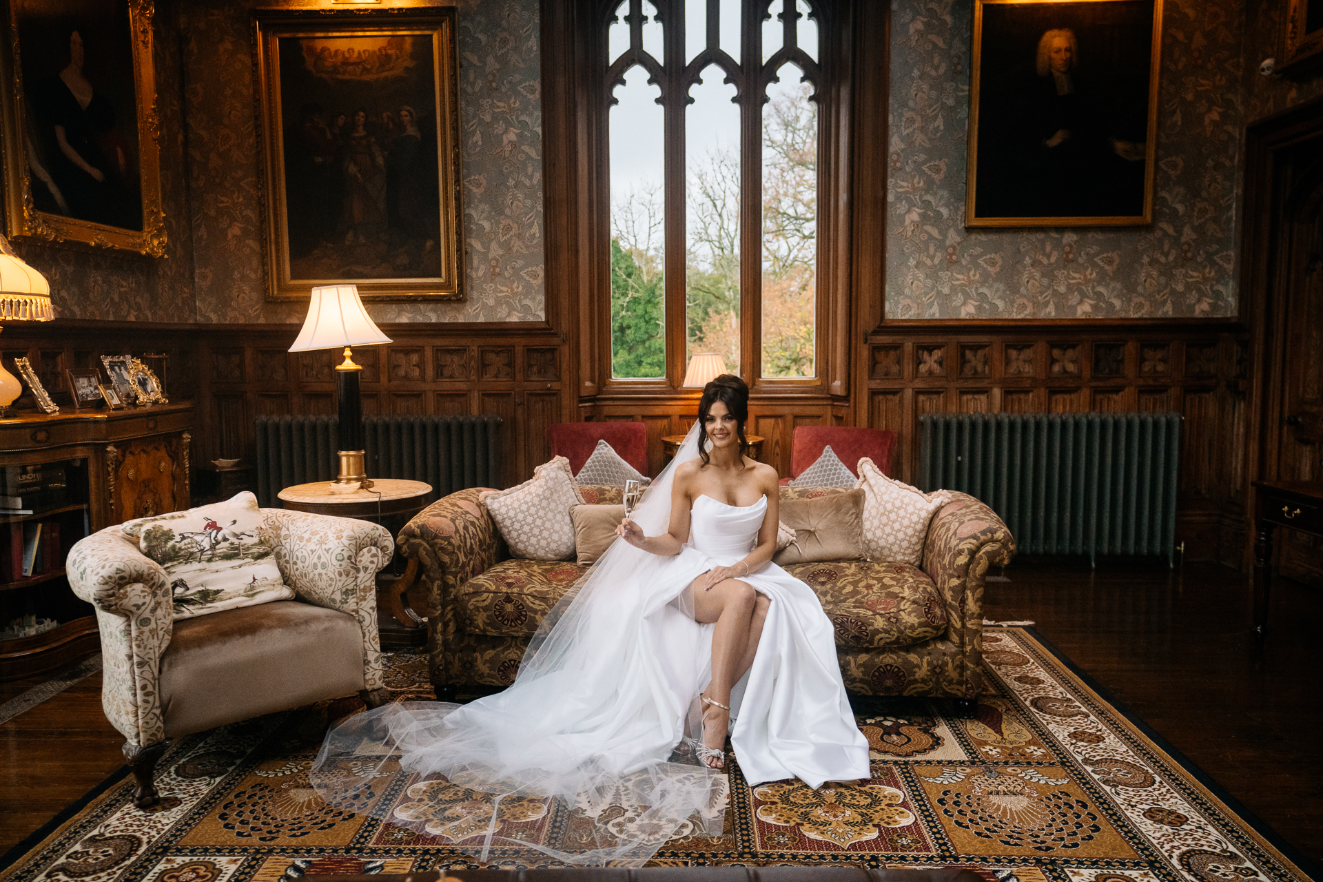 Bride in a white wedding dress sitting on an antique sofa in the Billiard Room of Markree Castle, surrounded by vintage décor and window light.