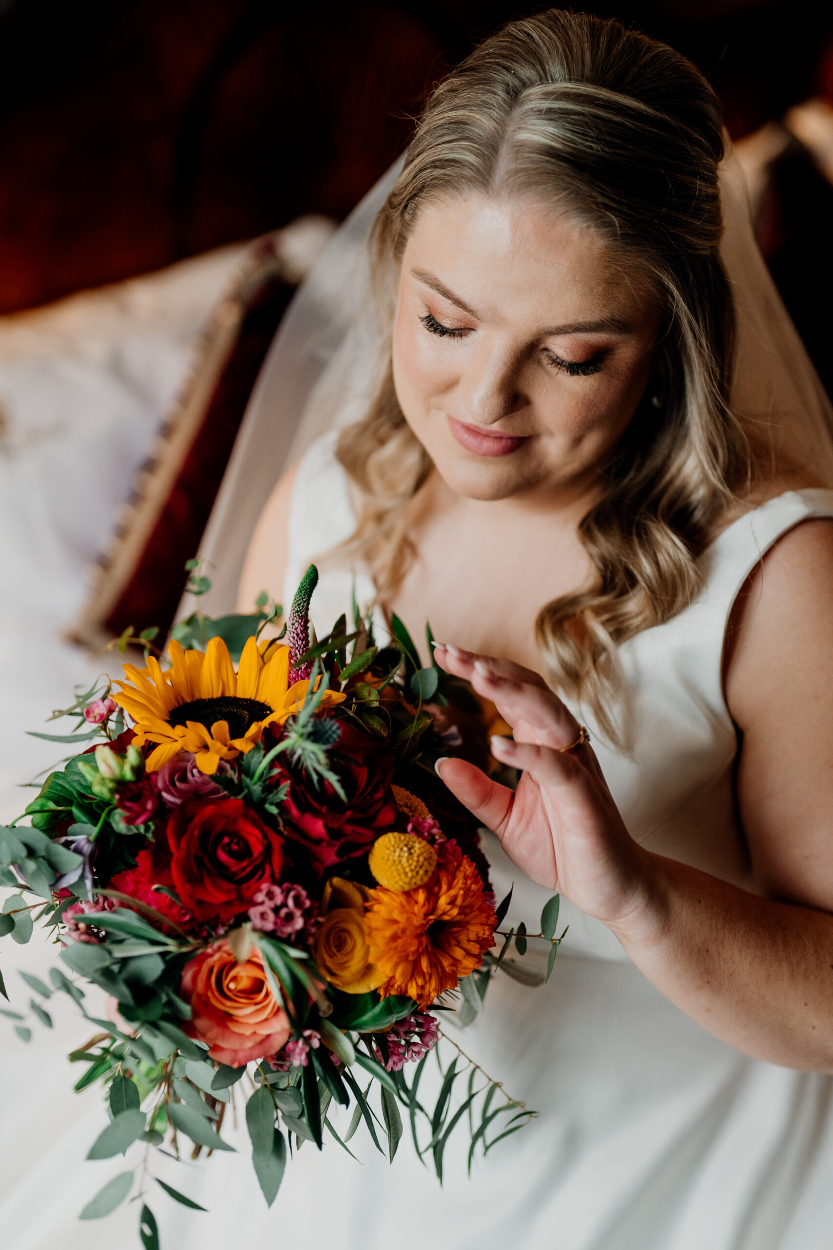 Bride holding a vibrant bouquet while sitting on the bed in the bridal suite at Markree Castle, with natural window light falling on her face.
