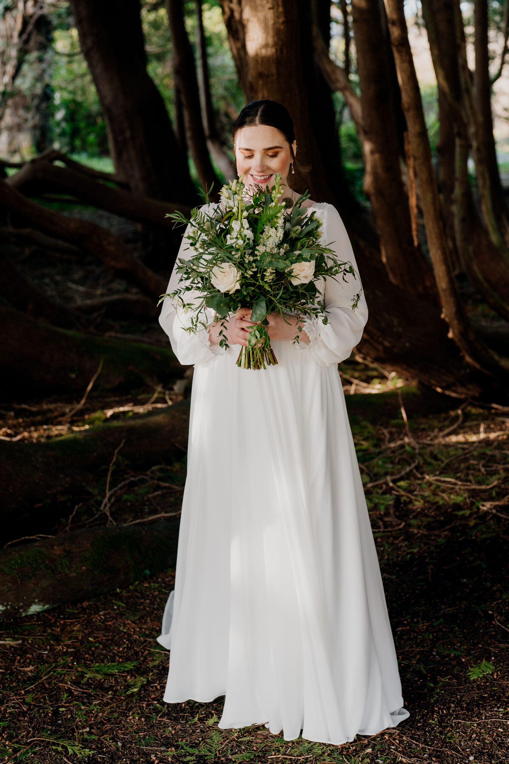 Bride standing in the forest garden of Markree Castle, holding a wild bouquet – romantic portrait captured for a destination wedding in Ireland.