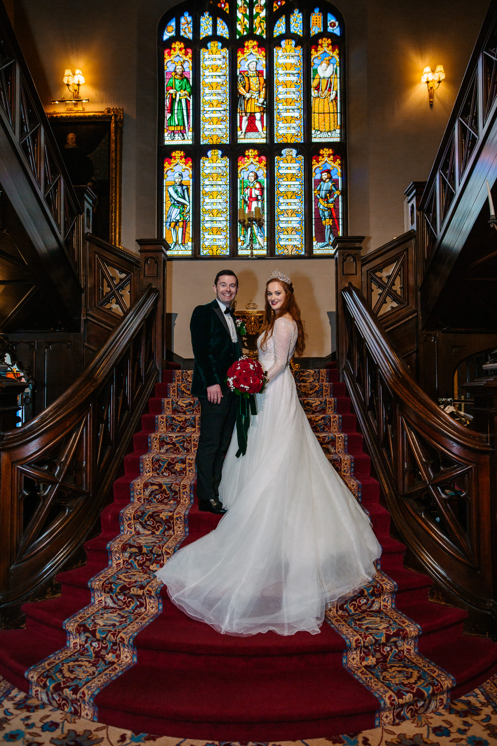 Couple standing on the red carpet staircase of Markree Castle with stained glass in the background.