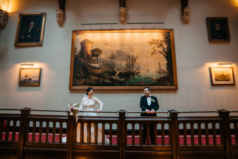 Bride and groom captured on the iconic balcony at Markree Castle, framed by a grand maritime painting and cinematic golden light – elegant Irish wedding moment.
