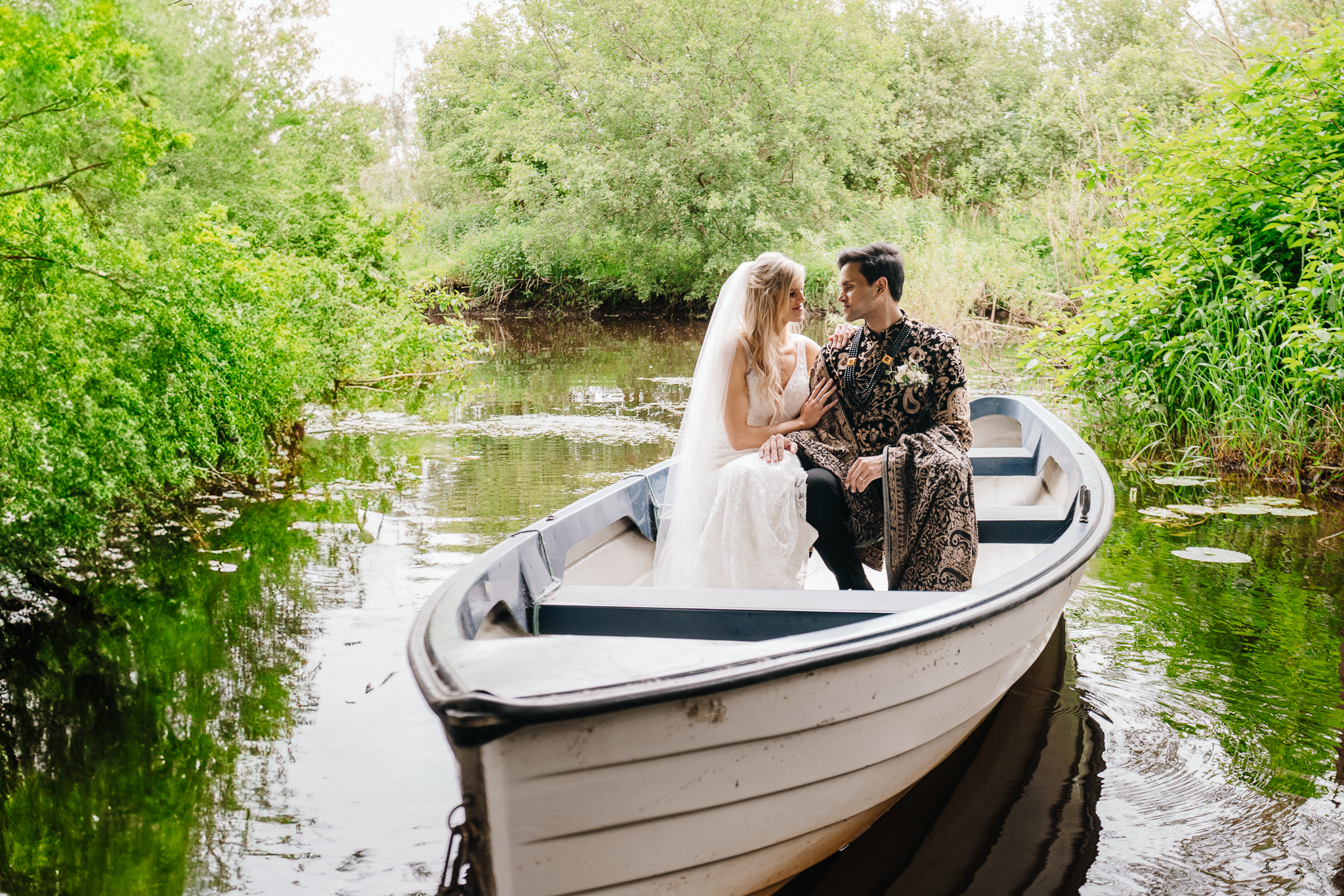 Bride and groom sitting in a white boat on the river surrounded by greenery during Markree Castle wedding – elegant and serene wedding portrait