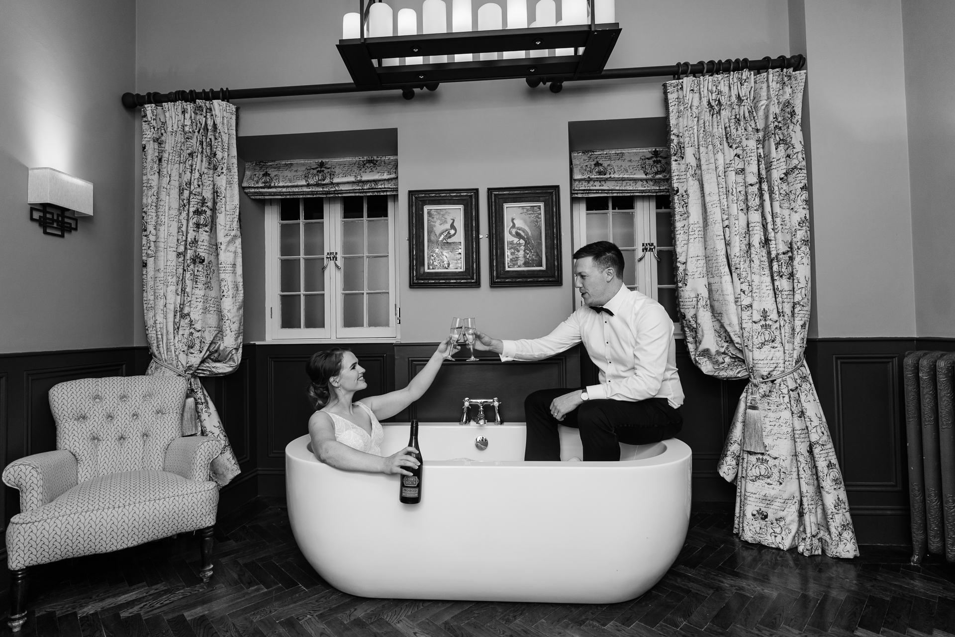 Bride and groom sharing a toast while sitting in a bathtub inside the bridal suite at Markree Castle – a candid and romantic black and white wedding portrait.