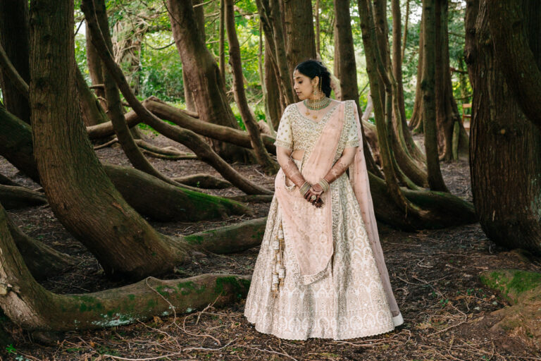 Indian bride in pastel lehenga standing among twisted forest trees at Markree Castle, Ireland – elegant bridal portrait in natural light