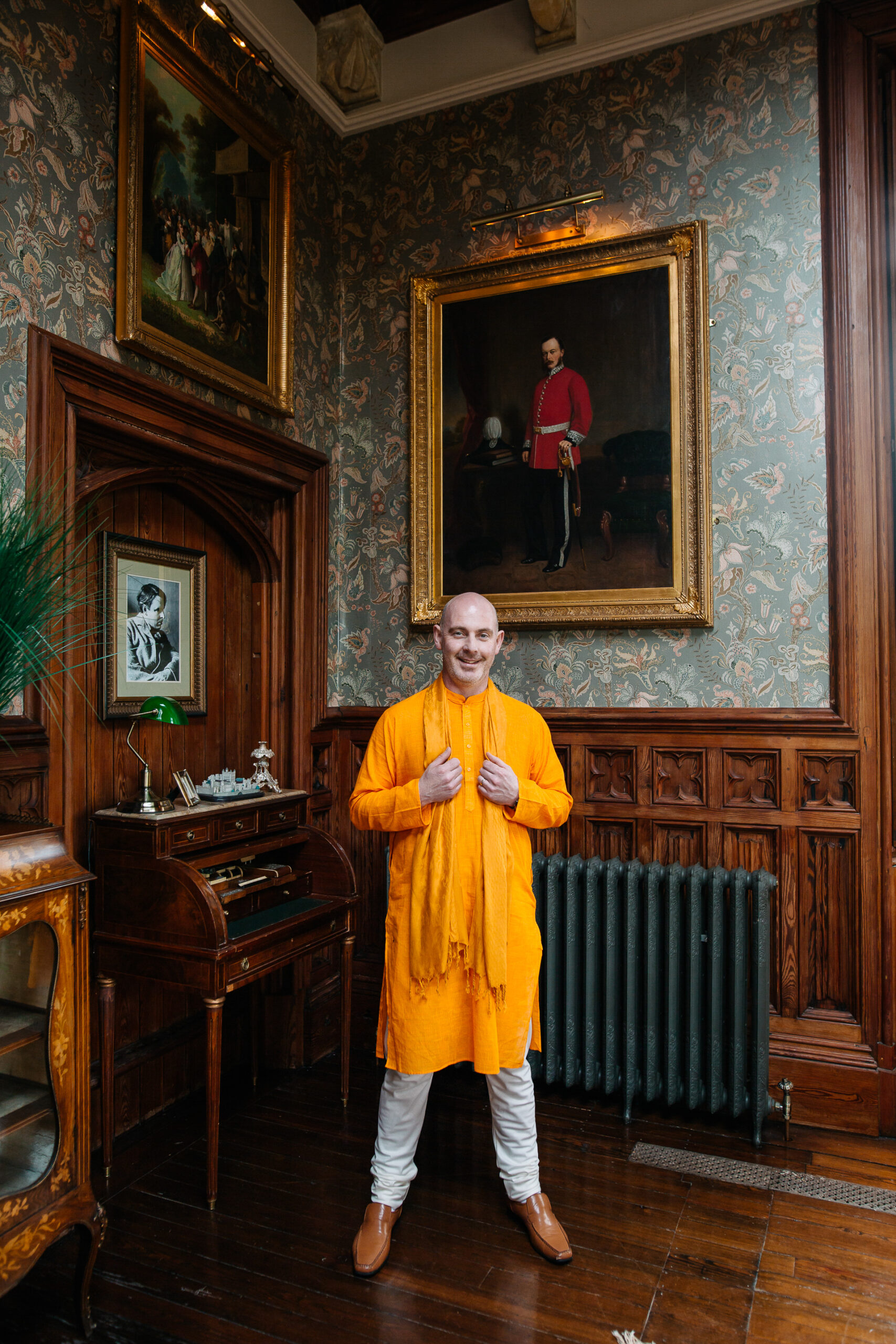The groom poses in a traditional orange kurta at Markree Castle, framed by classic wooden interiors and vintage paintings