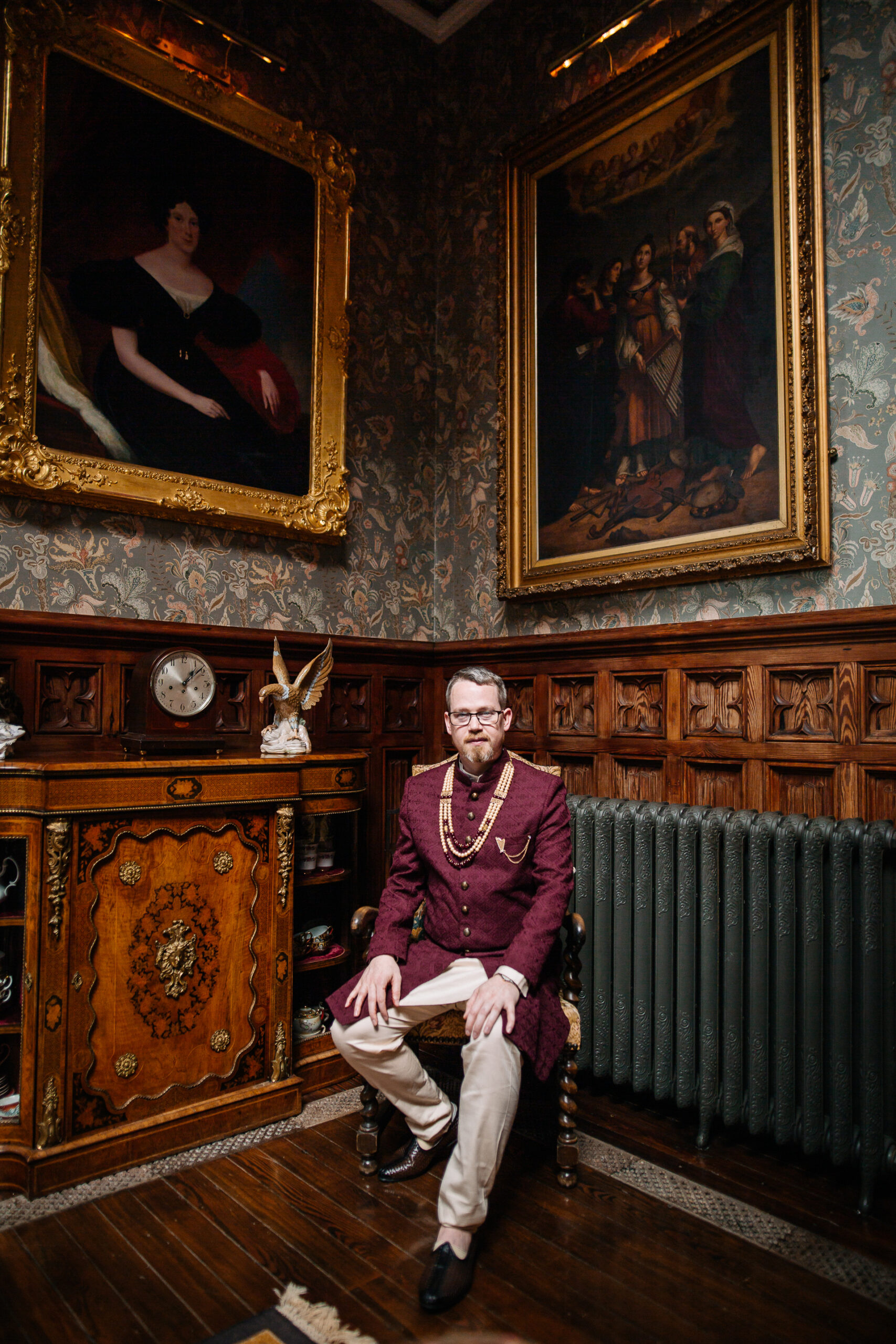 Groomsman sitting in a vintage room wearing a burgundy kurta at Markree Castle wedding