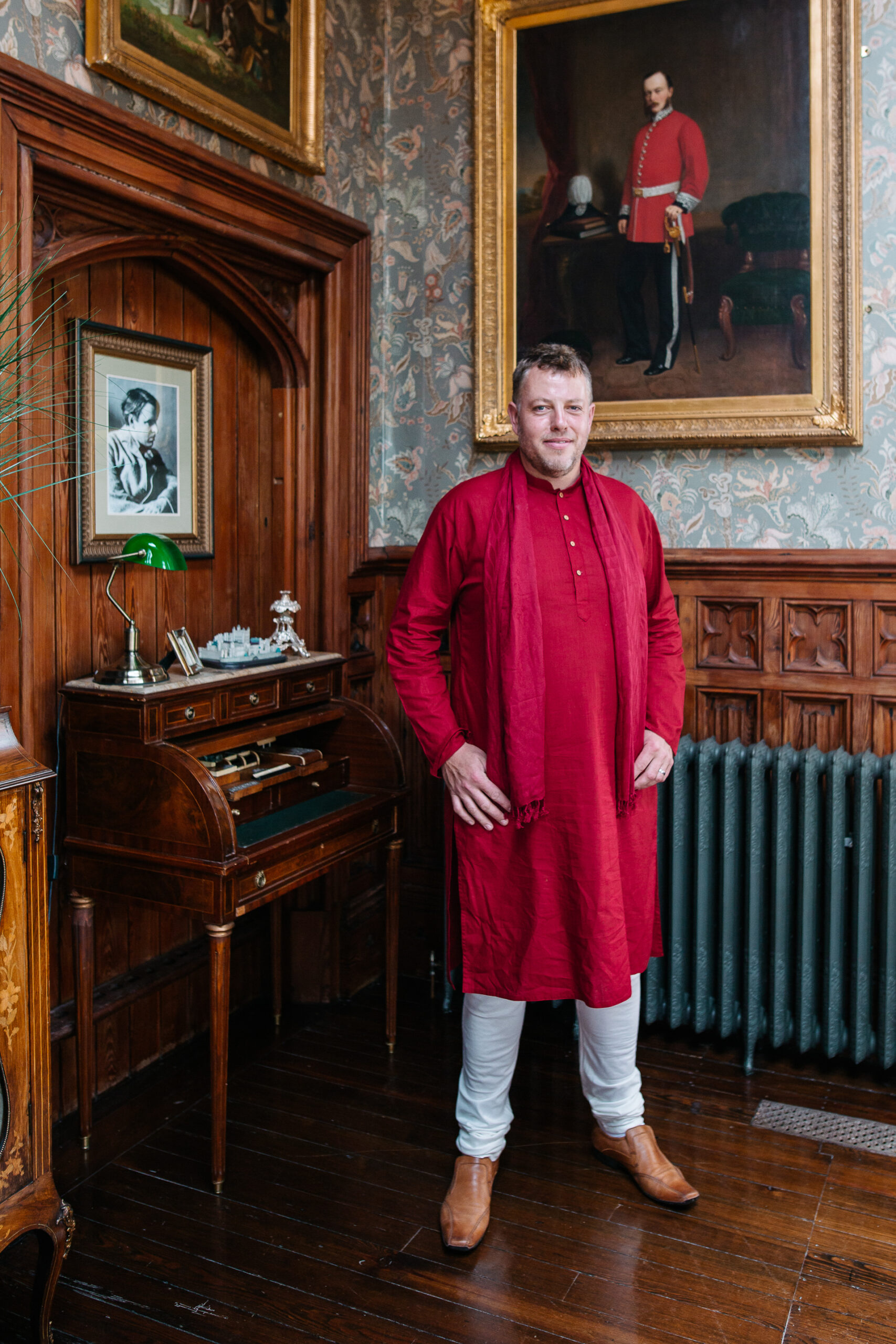 Groomsman in a red kurta posing confidently in a wood-panelled room at Markree Castle wedding