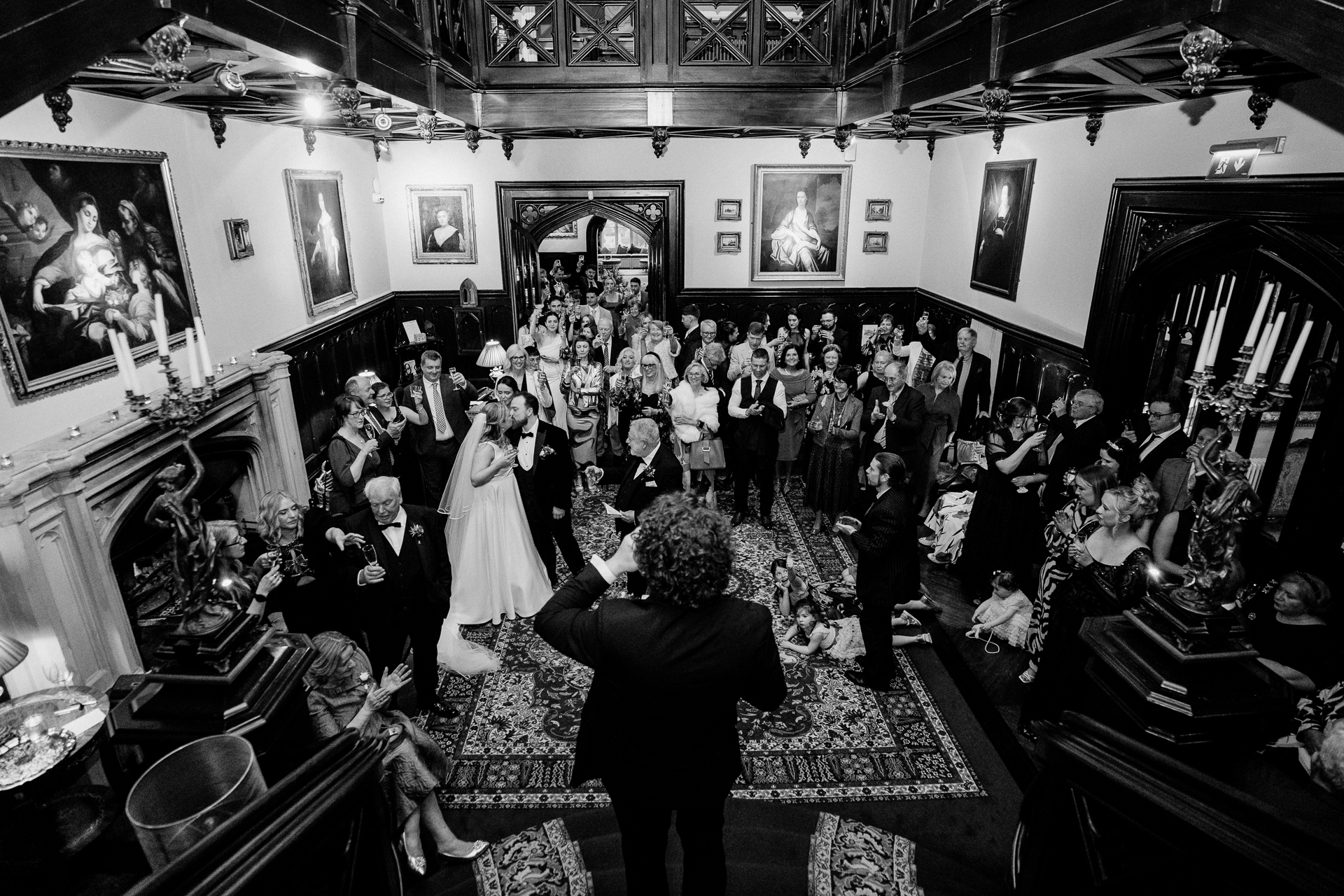 Black and white photo of a joyful wedding toast at Markree Castle reception with guests watching from the staircase