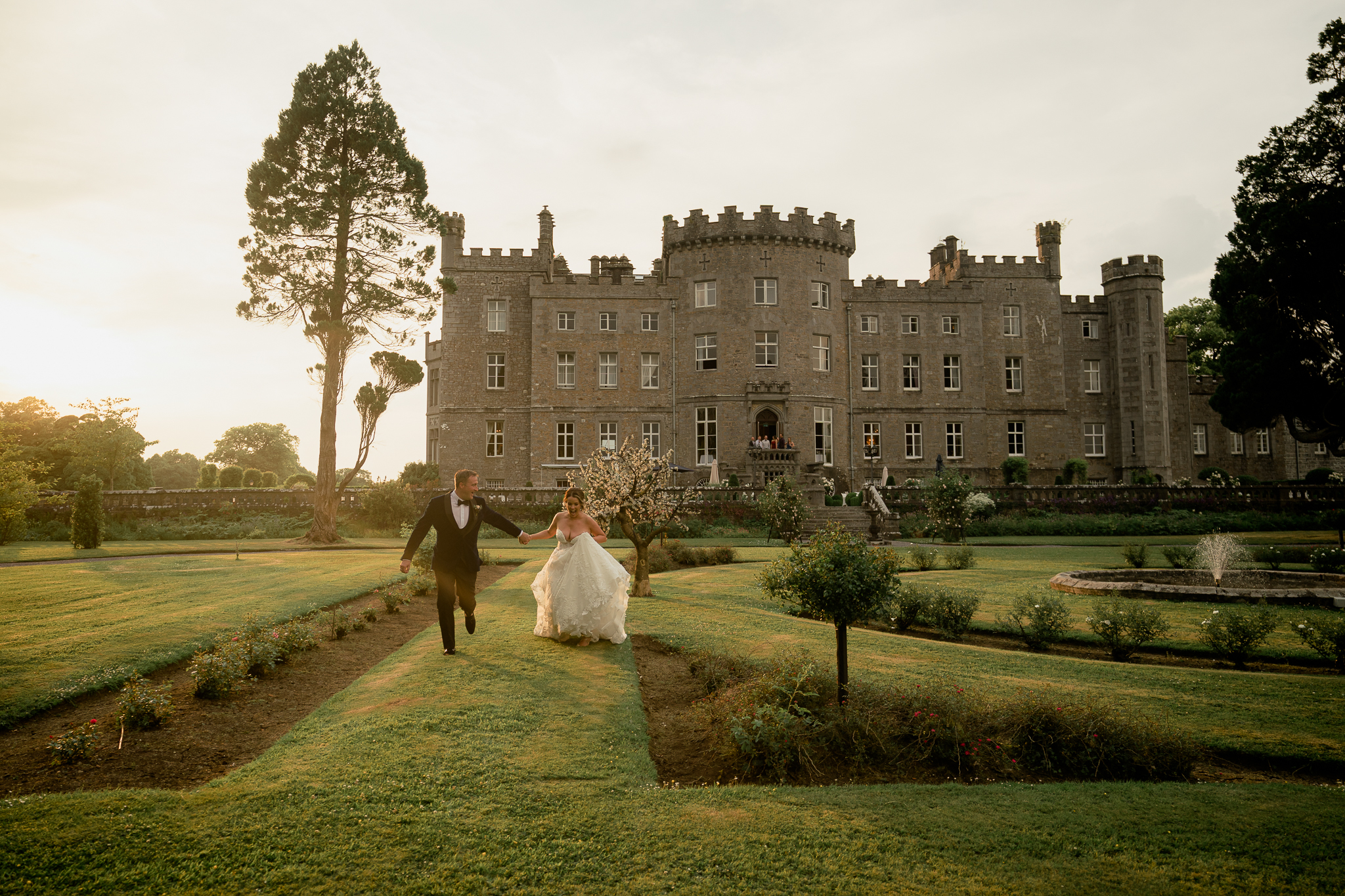 Bride and groom walking along the garden path of Markree Castle in soft sunset light during their destination wedding in Ireland