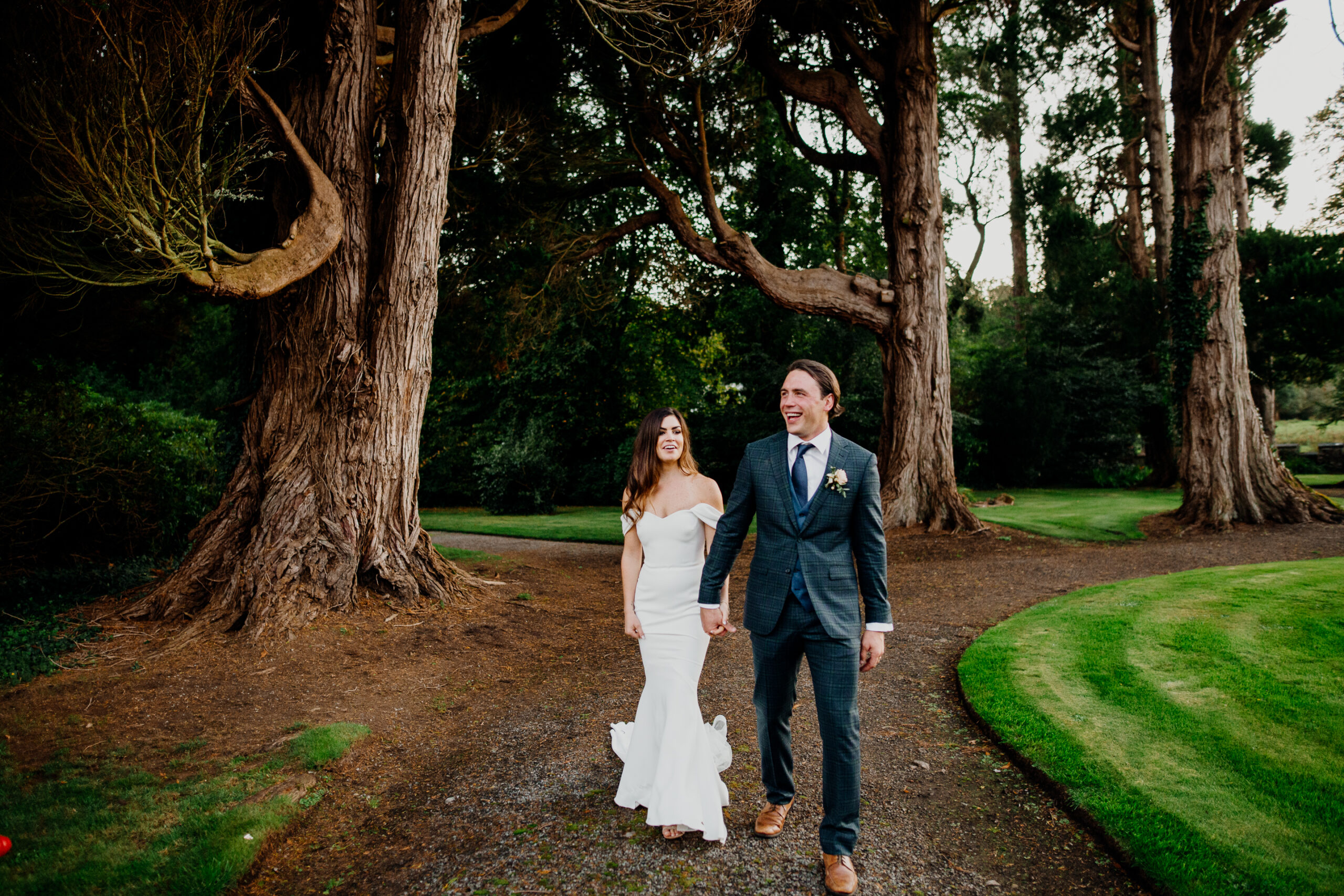 Bride and groom walking hand in hand under tall trees at Markree Castle during a wedding portrait session