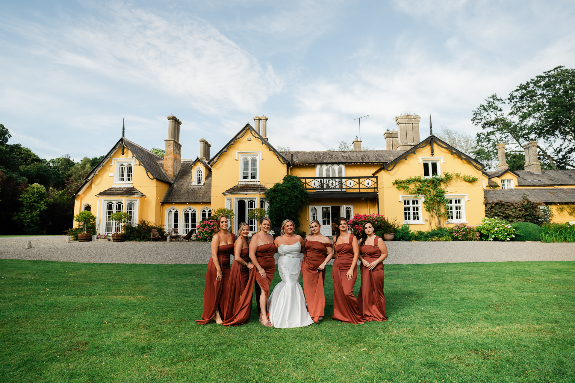 Bridal party in burgundy dresses posing in front of Martinstown House on wedding day