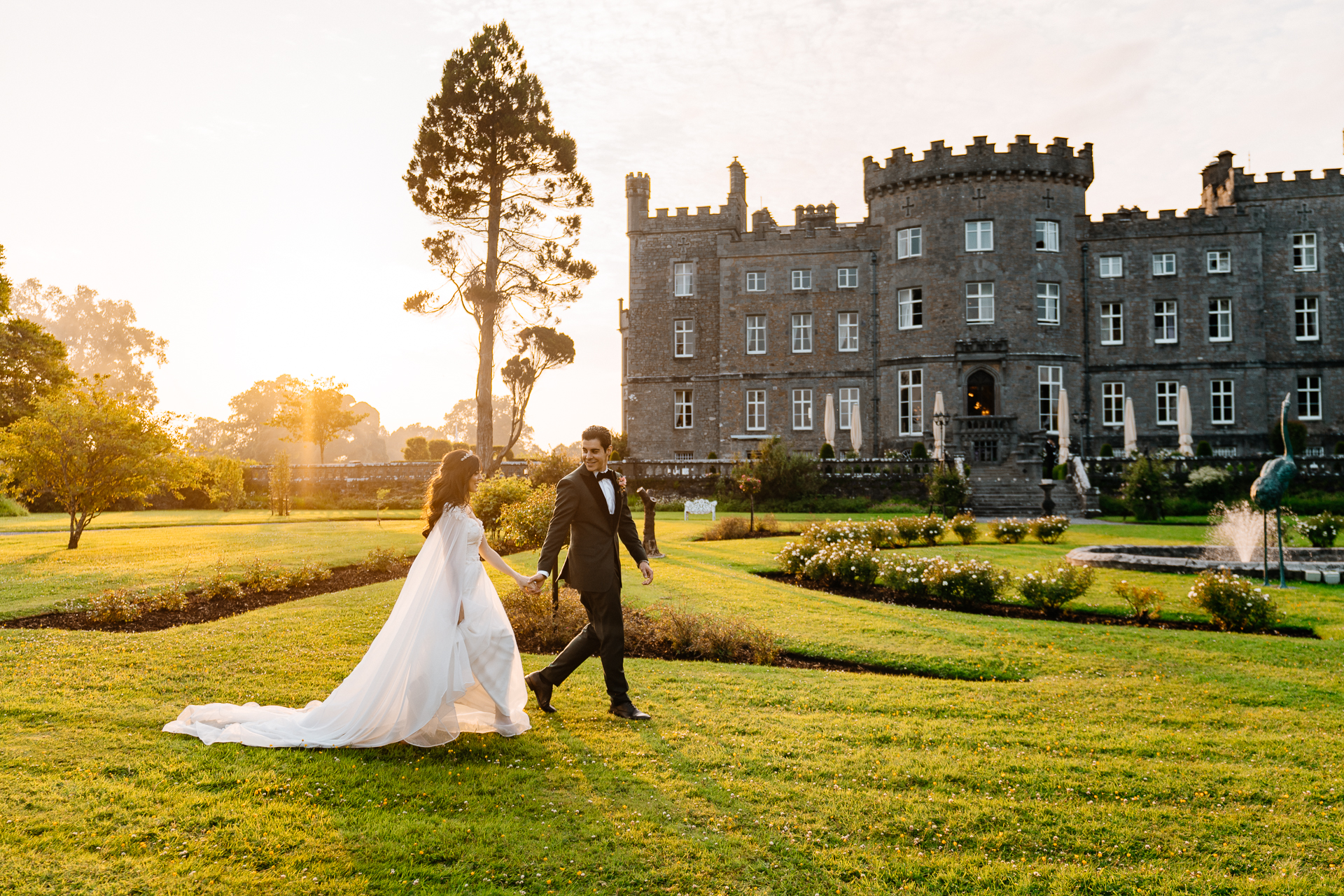 Bride and groom walking hand in hand across the lawn at Markree Castle during golden hour sunset


