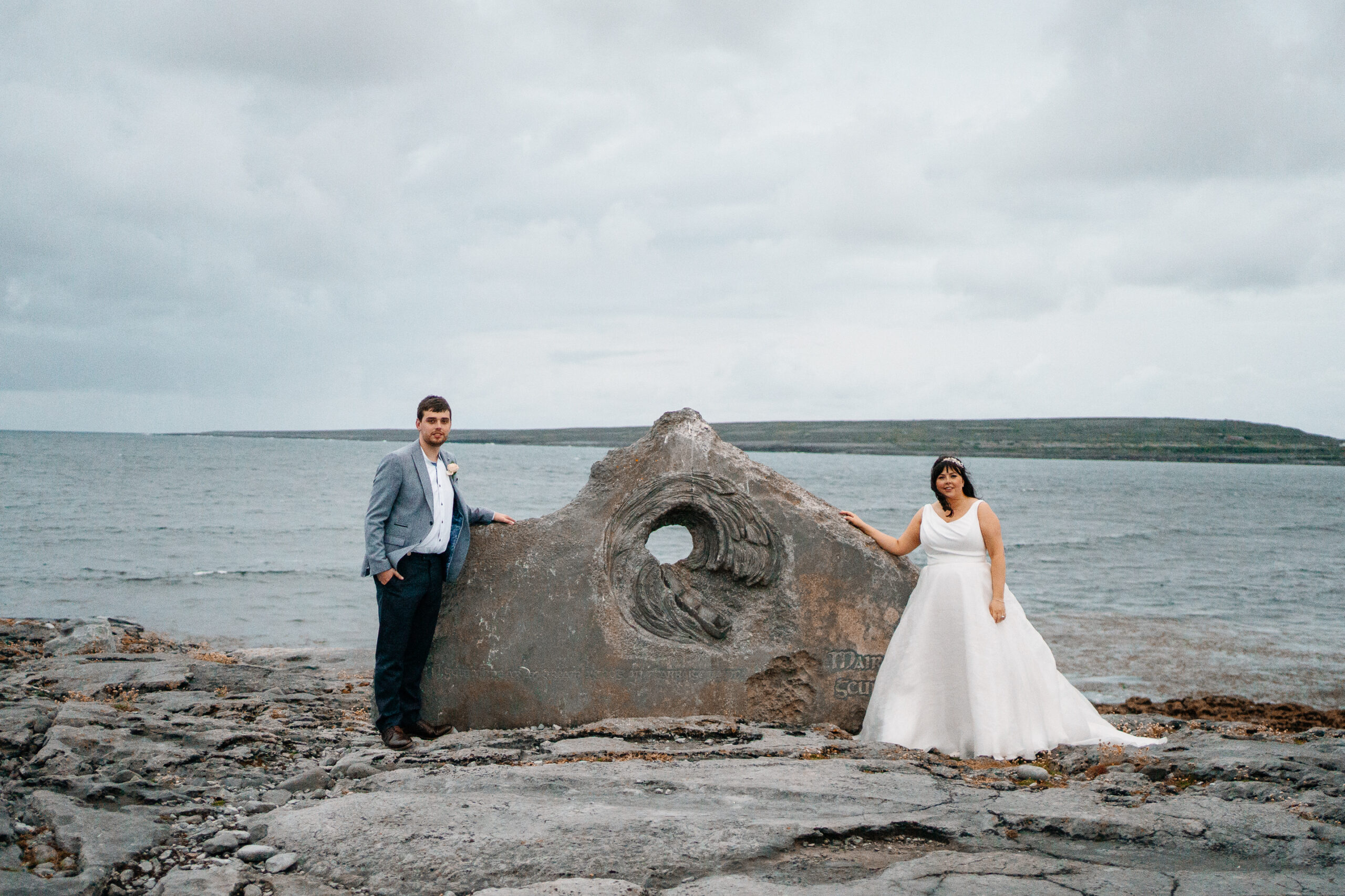 Bride and groom standing by the memorial stone near Inisheer harbour – wild wedding scenery on Aran Islands
