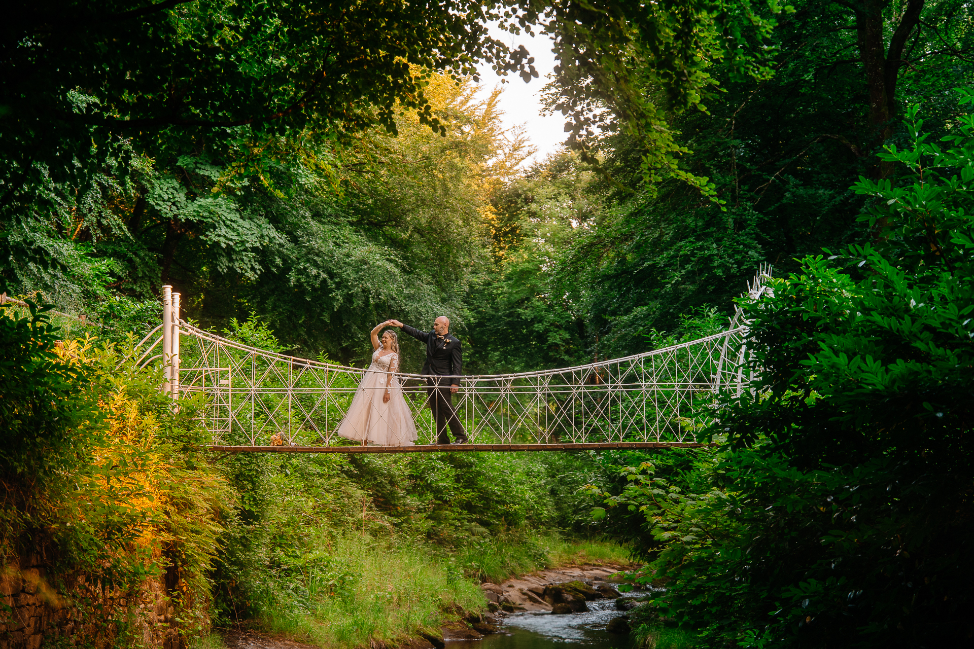Bride and groom walking across Kinnitty Suspension Bridge and forest paths at sunset near Kinnitty Castle Hotel.