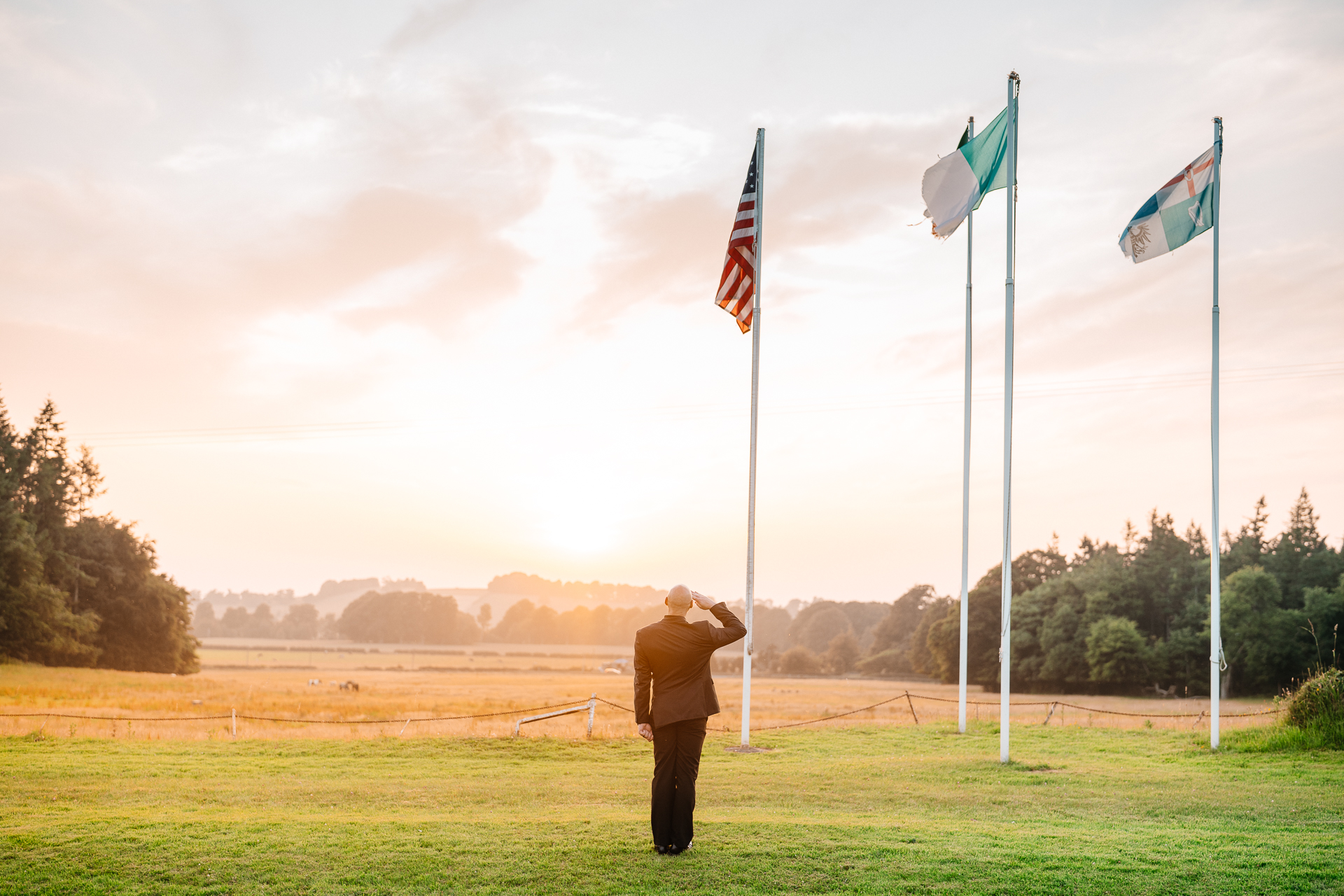 Groom standing under Irish and US flags at sunset – Kinnitty Castle Hotel wedding