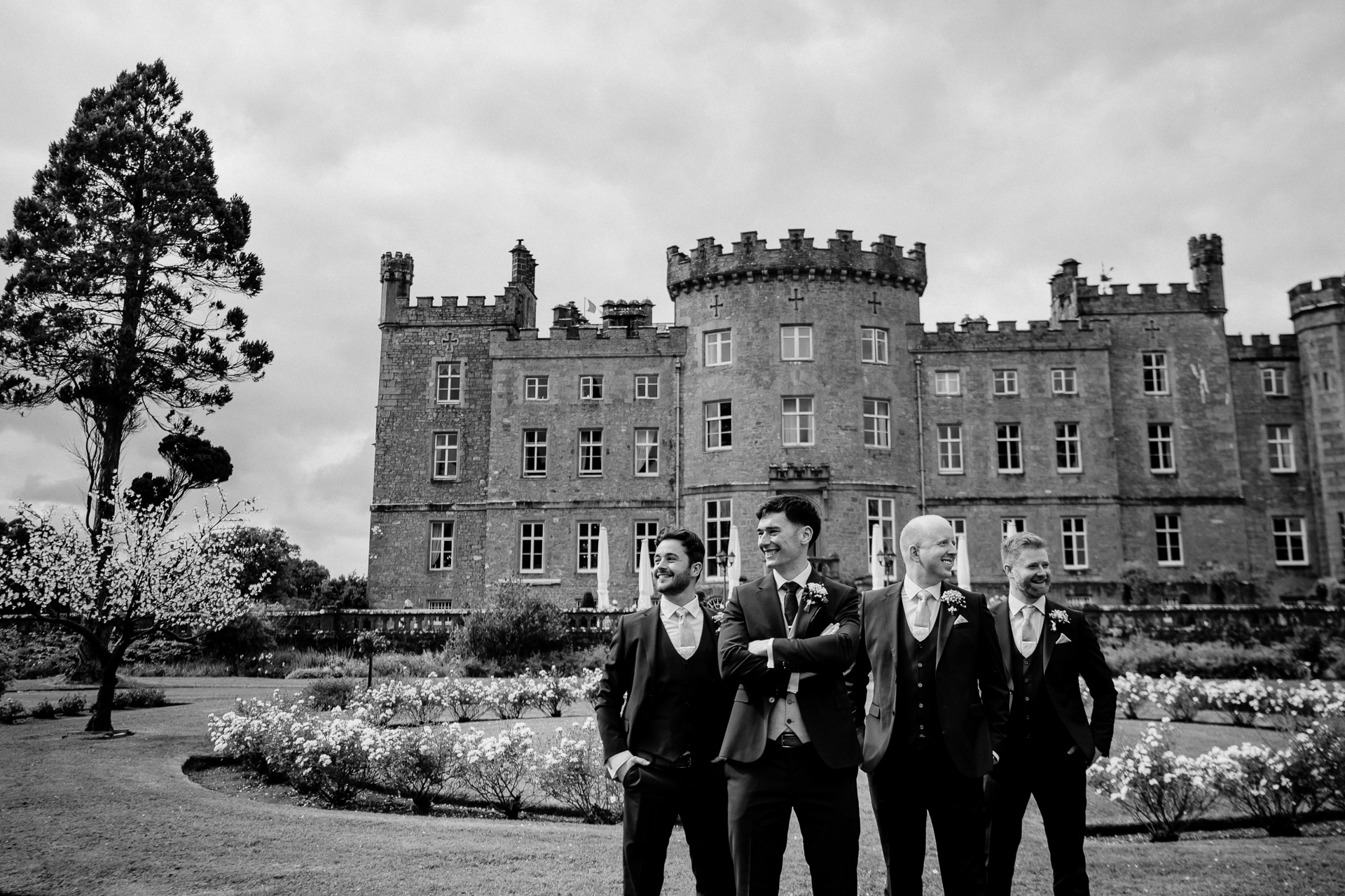 Groom and groomsmen in tuxedos standing in front of Markree Castle – black and white wedding photo

