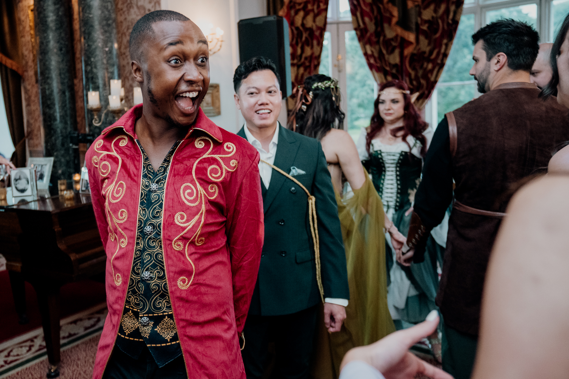 Man in a red fantasy-style coat smiling and chatting with other guests during a rehearsal dinner at Markree Castle, Sligo, Ireland