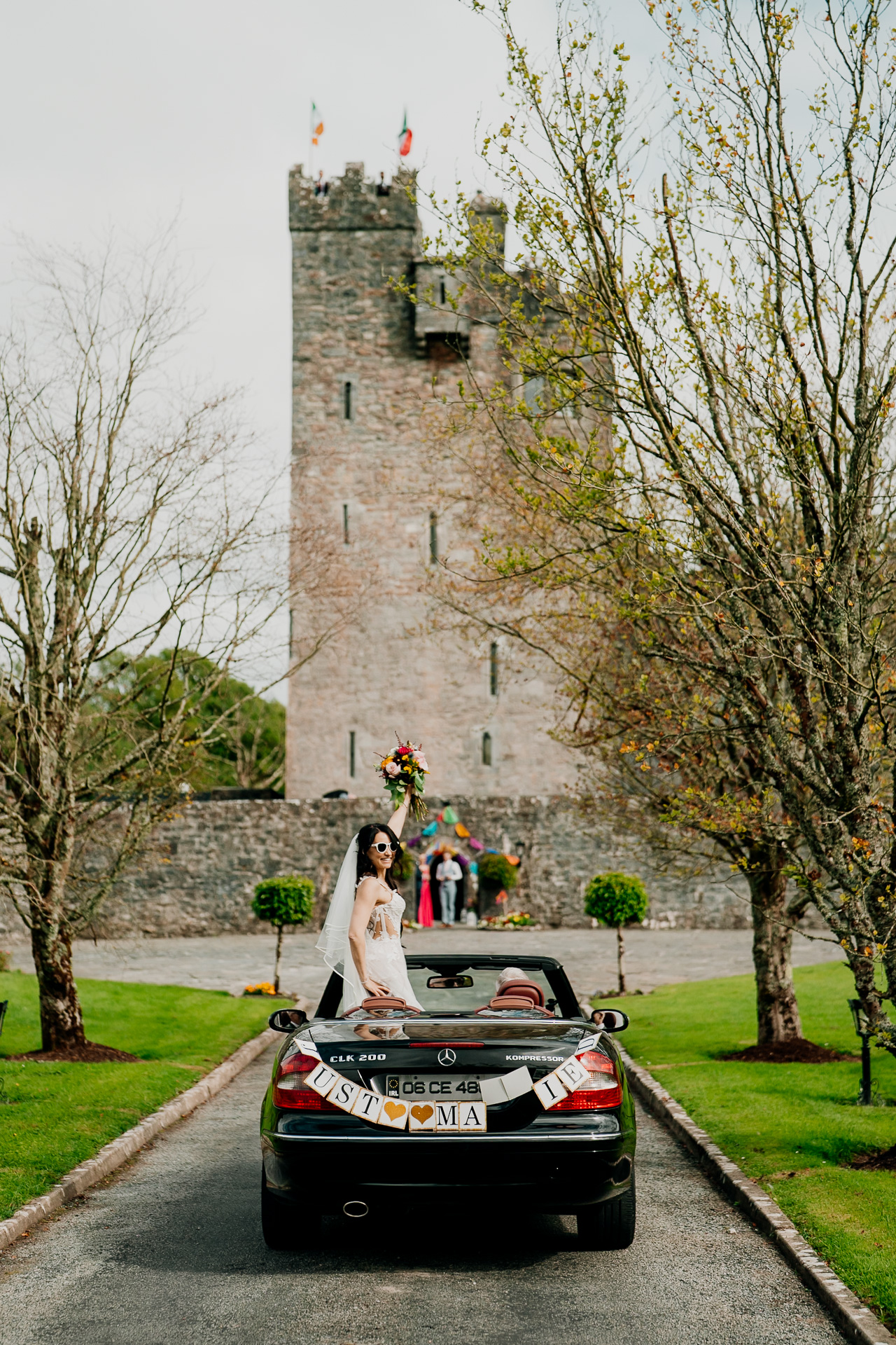 Bride and groom in a convertible in front of Cloughan Castle in County Galway