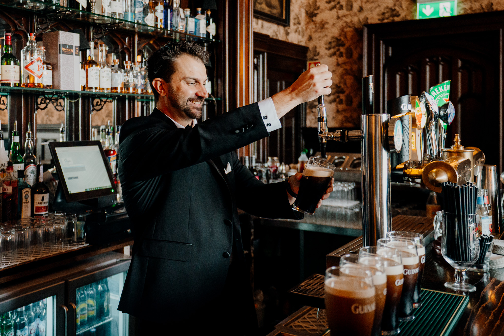 Groom pouring a drink at the bar during wedding preparations at Markree Castle