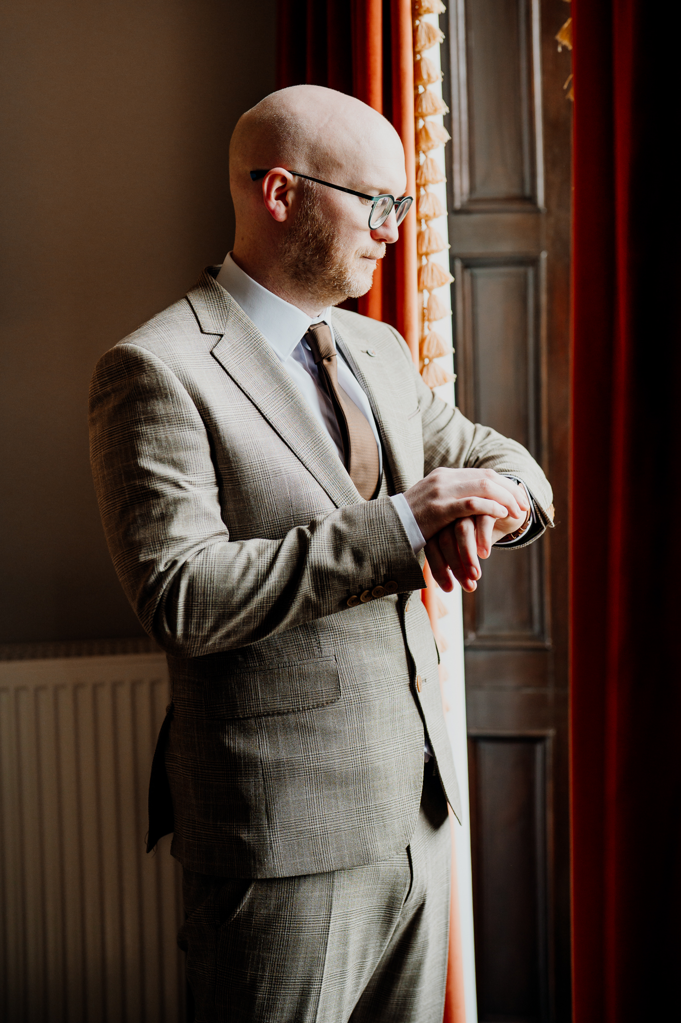 Groom adjusting his shirt cuff beside a window in the Johnny Cash Room at Markree Castle