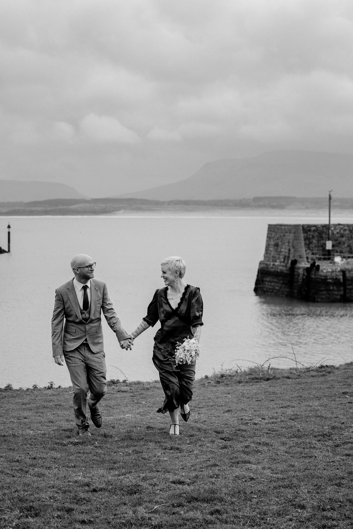 Black and white photograph of newlyweds walking beside Mullaghmore Harbour in County Sligo