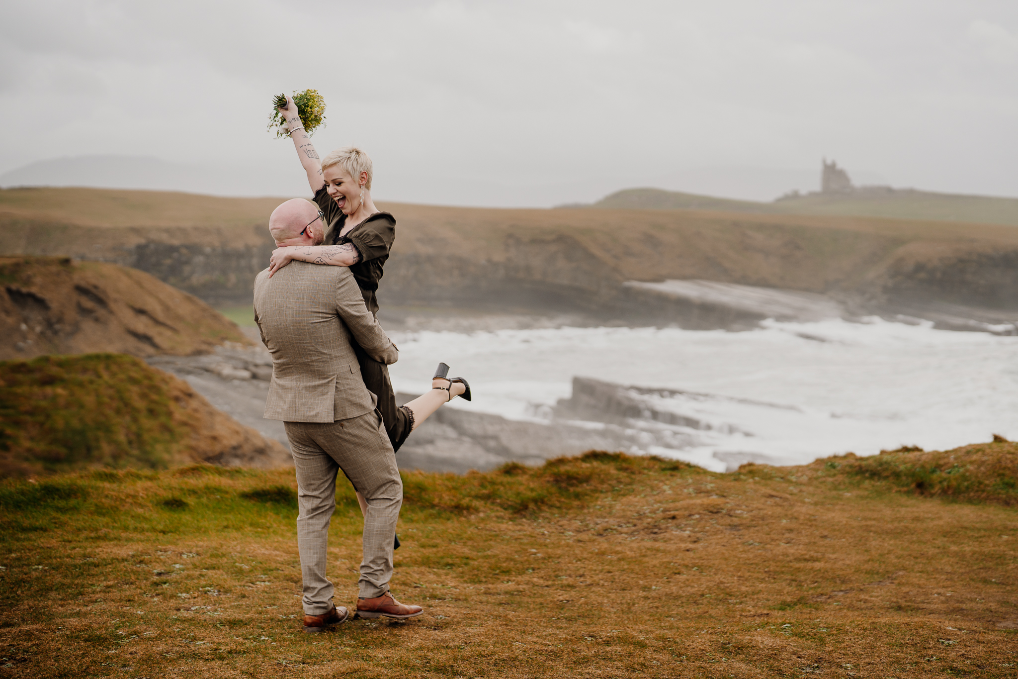 Groom lifting his bride at Mullaghmore Head with Classiebawn Castle visible in the distance
