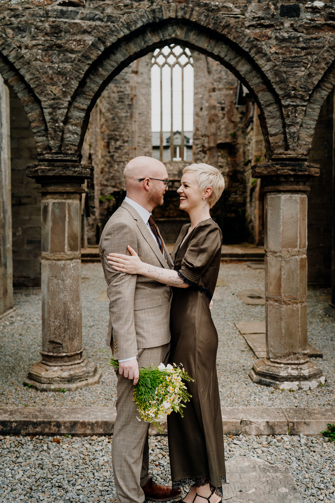 Intimate wedding couple embracing beneath a medieval stone arch at Sligo Abbey
