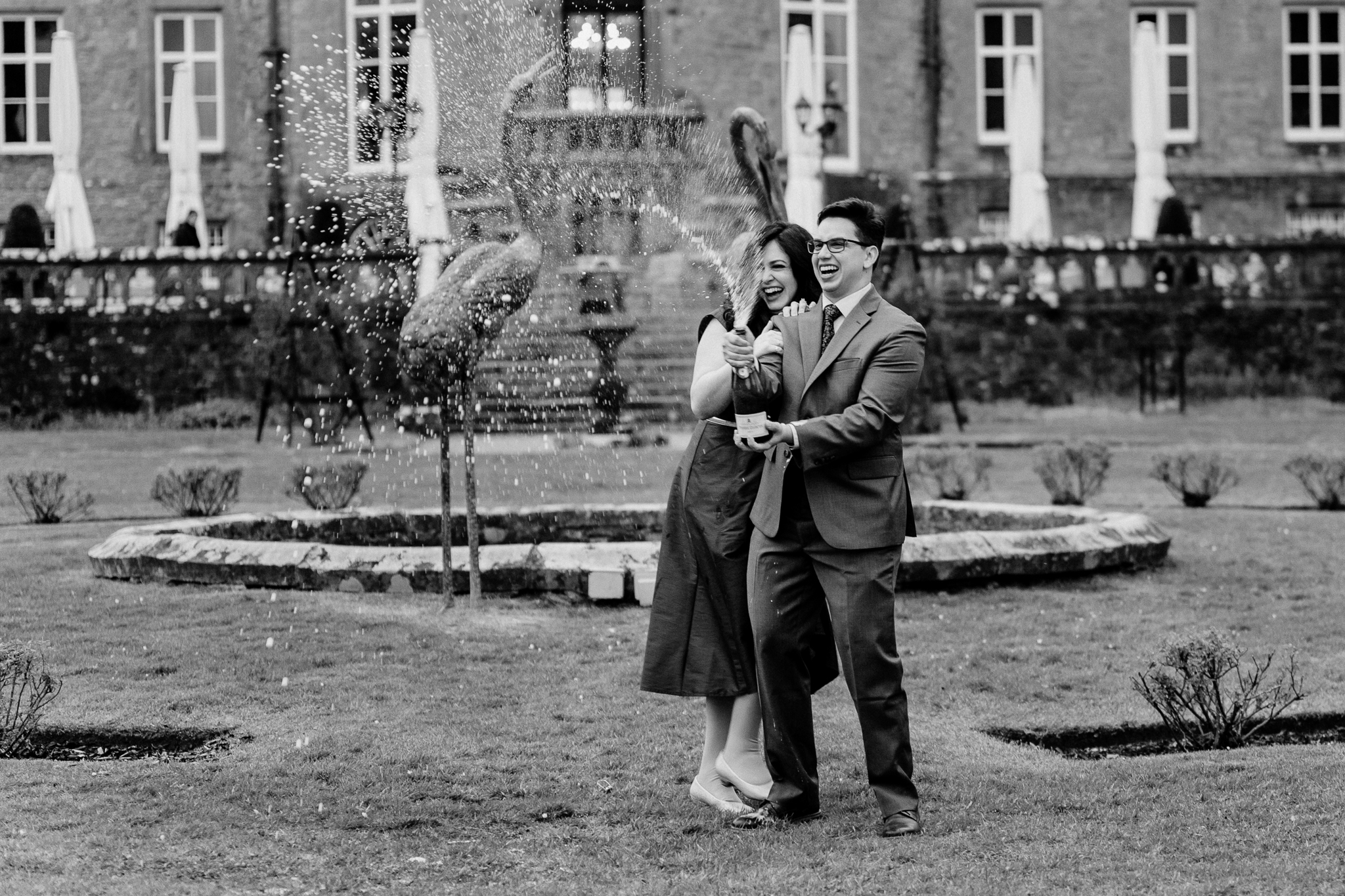 Black-and-white photograph of a newly engaged couple celebrating with champagne in front of Markree Castle in Sligo, Ireland.