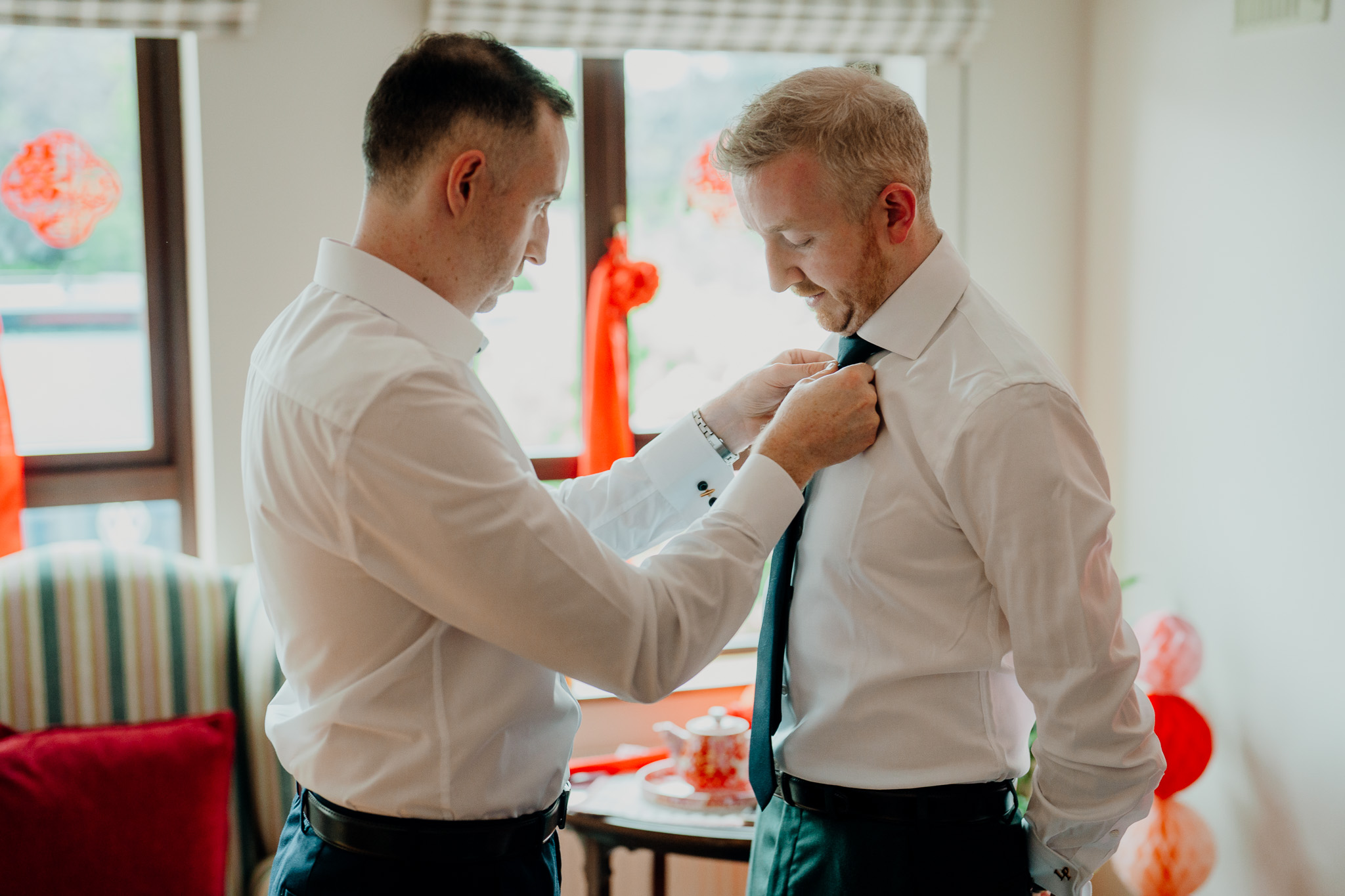 Groom getting dressed with help during wedding morning preparations