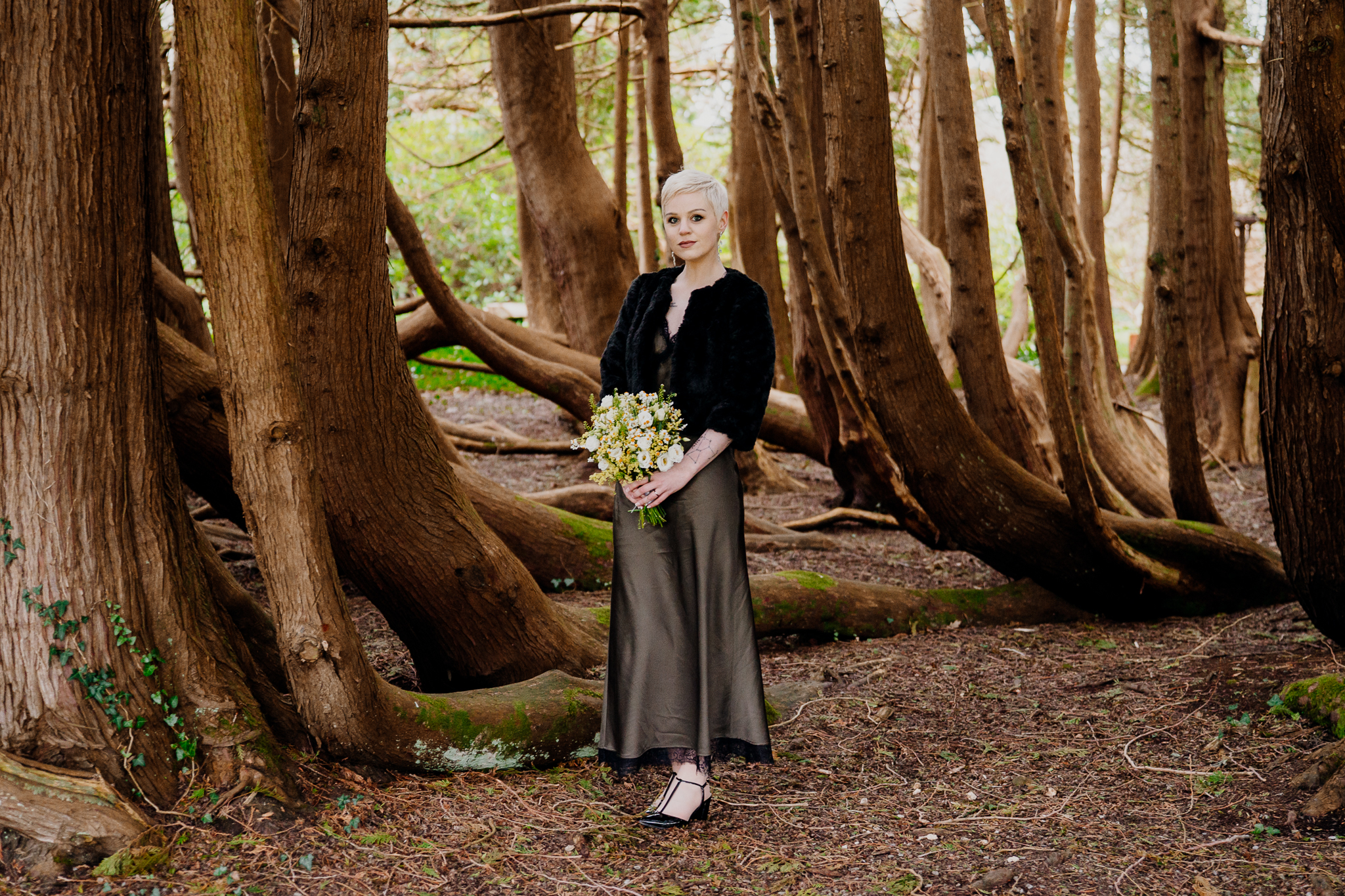 Bride holding her wedding bouquet among mature trees in Markree Castle woodland Sligo
