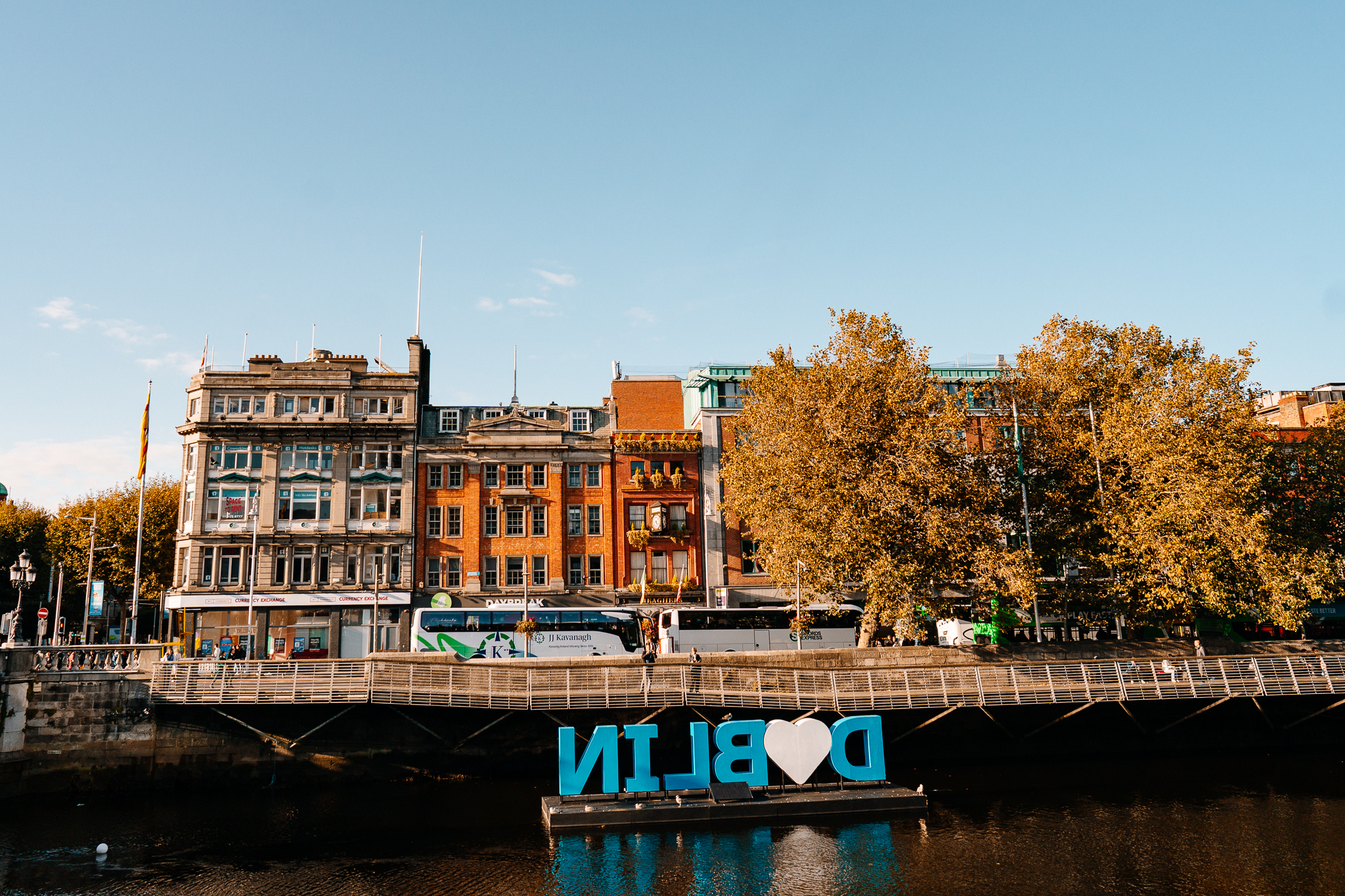 River Liffey waterfront in Dublin with historic buildings and autumn-coloured trees on a sunny afternoon