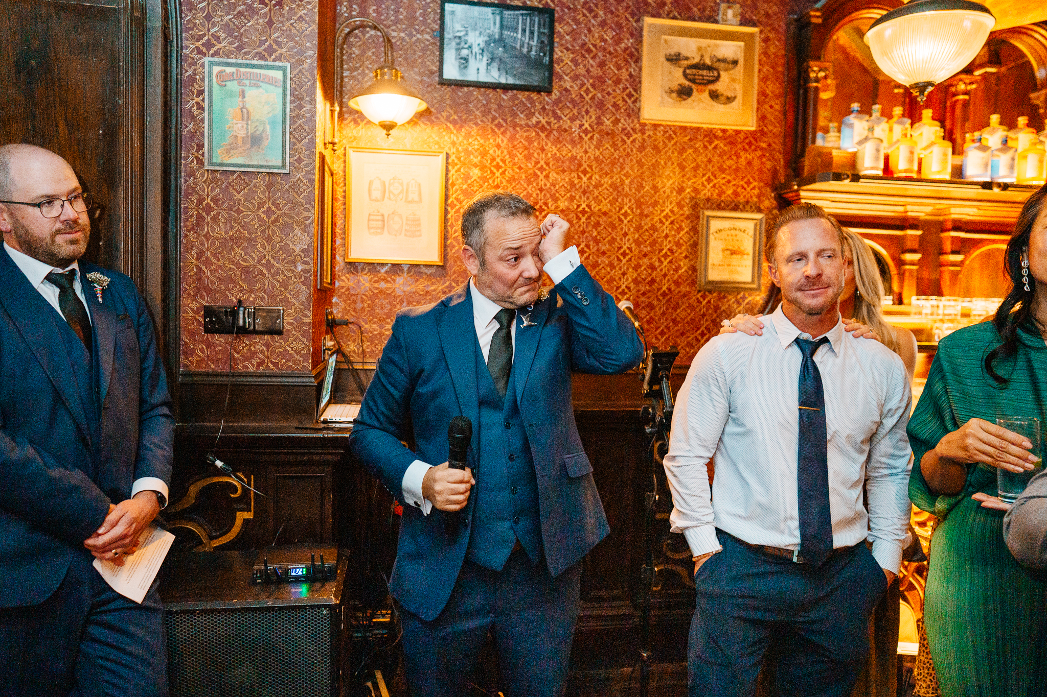 Man in a blue jacket delivering a wedding speech beside a seated woman at J.R. Mahon's pub in Dublin