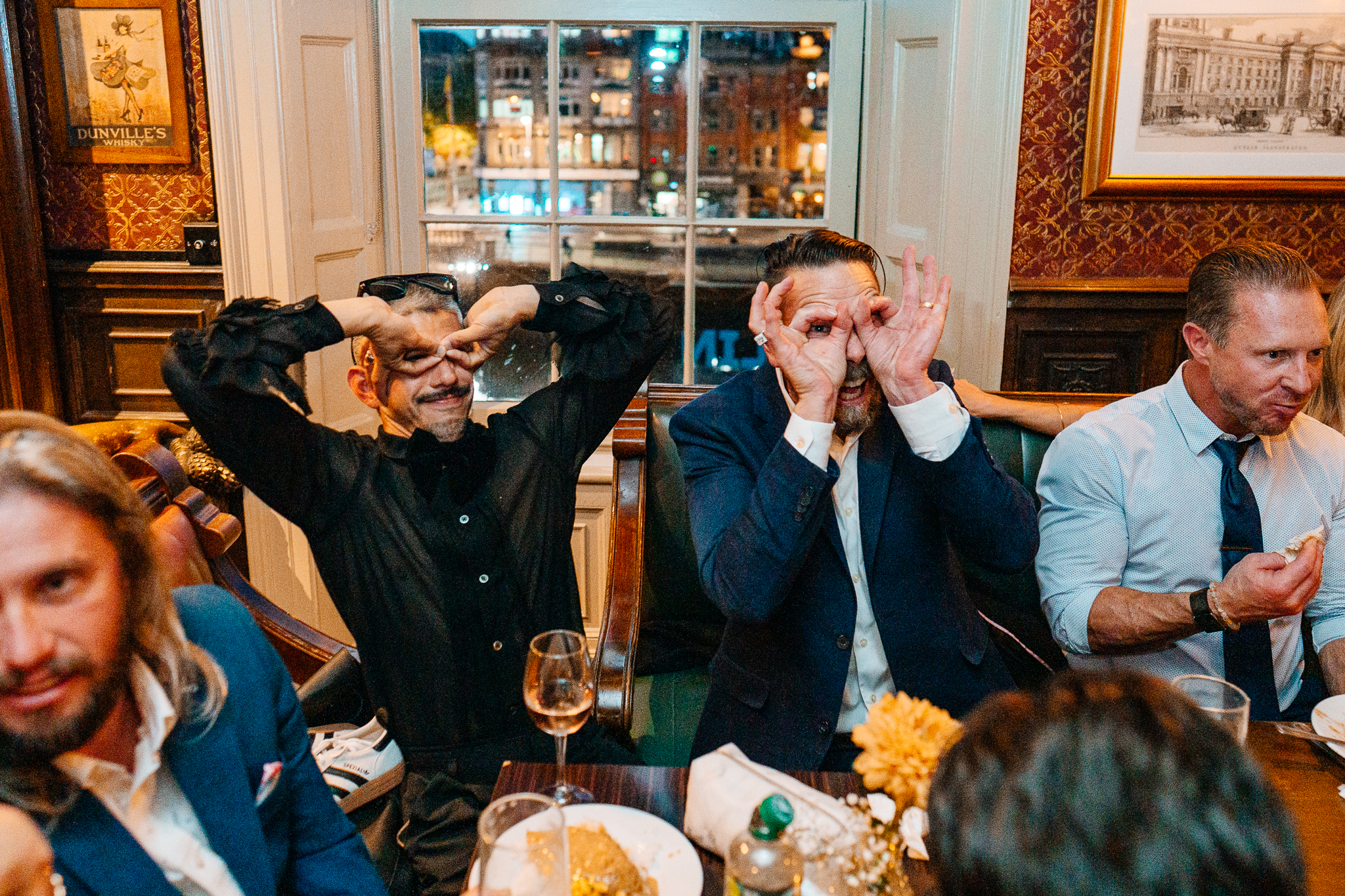 Two male wedding guests reacting emotionally while seated at a table during a Dublin wedding reception