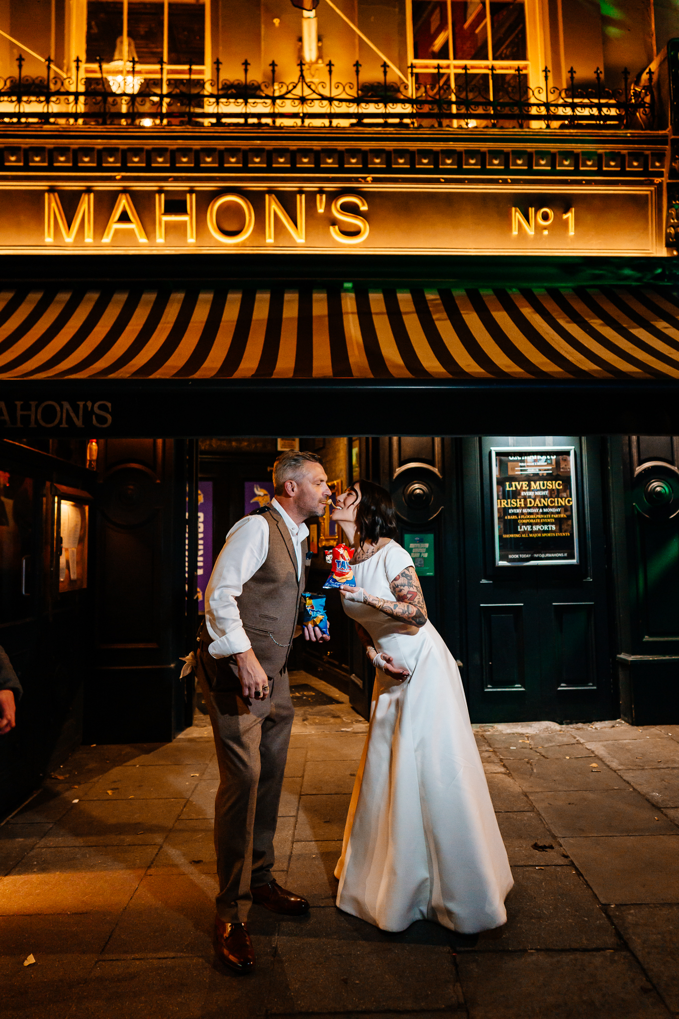 Bride and groom standing beneath the illuminated Mahon's pub sign during their wedding night in Dublin