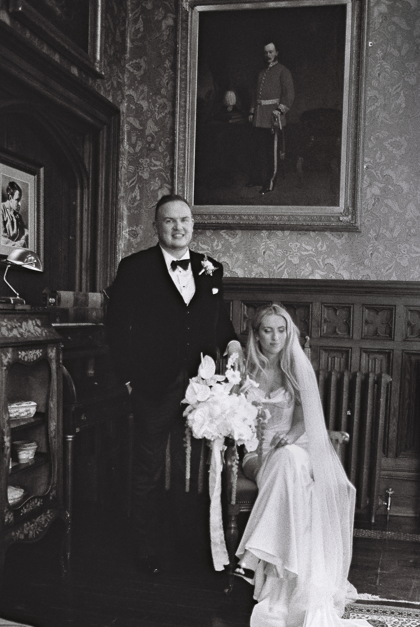 Black and white 35mm film wedding portrait of a seated bride with the groom standing beside her in the historic Billiard Room at Markree Castle, Sligo.
