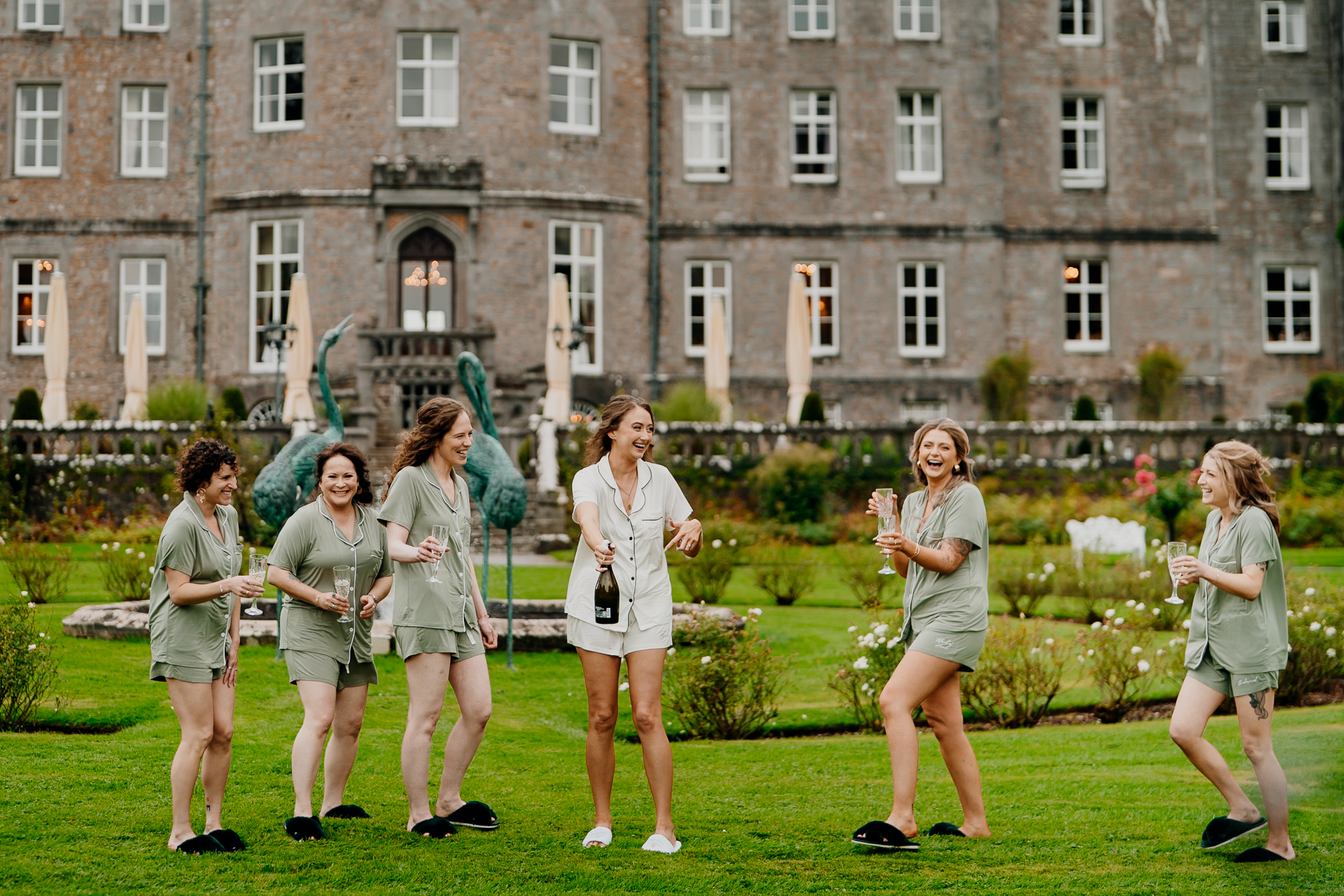 Bride and bridesmaids celebrating with champagne in the gardens outside Markree Castle, with the historic castle behind them.