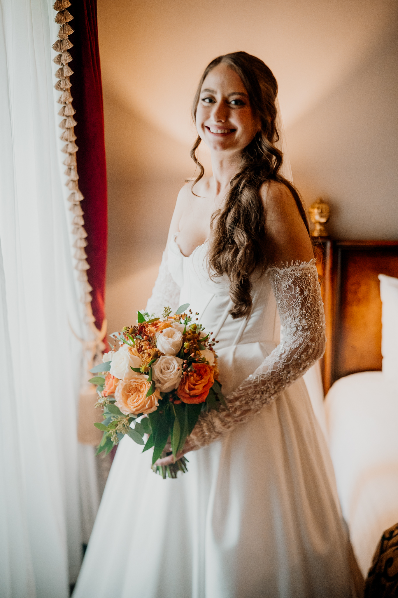 Bride standing in her wedding gown holding a colourful autumn bouquet beside a warm-toned interior at Markree Castle.