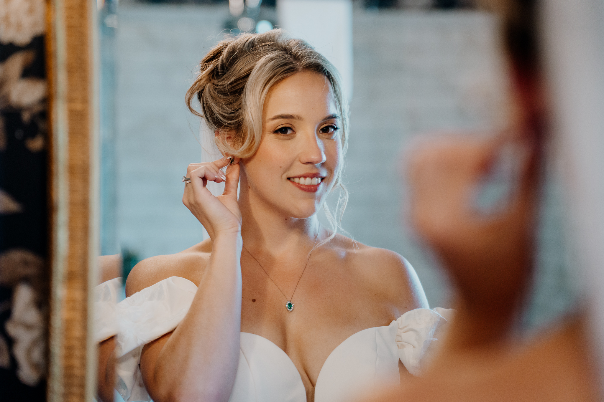 Smiling bride adjusting her wedding earrings in an off-the-shoulder bridal gown at Markree Castle, Sligo.