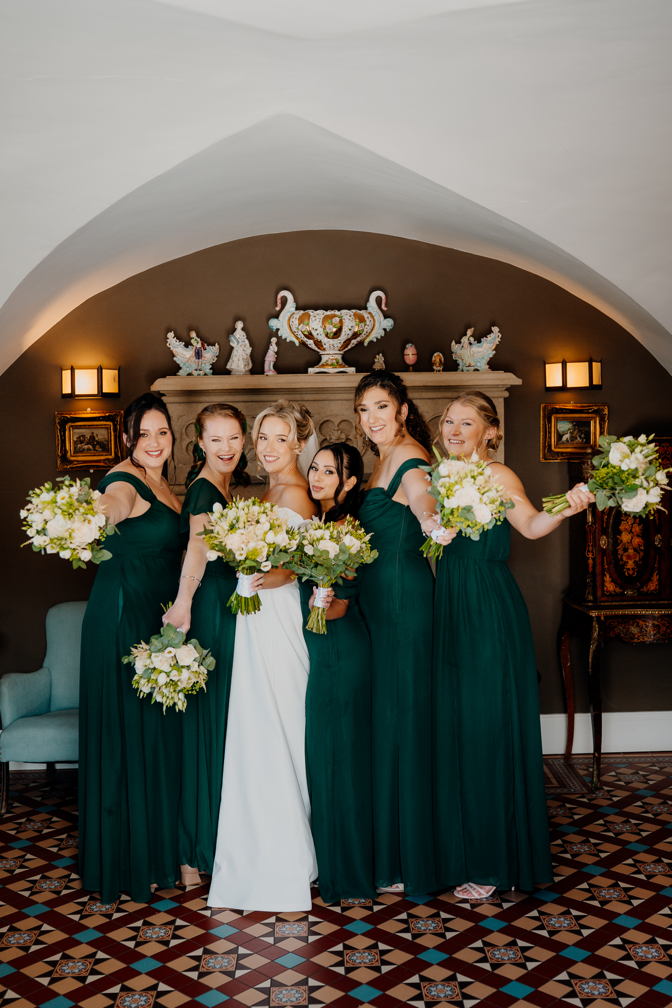 Bride and bridesmaids in green dresses posing together beneath an archway at Markree Castle.