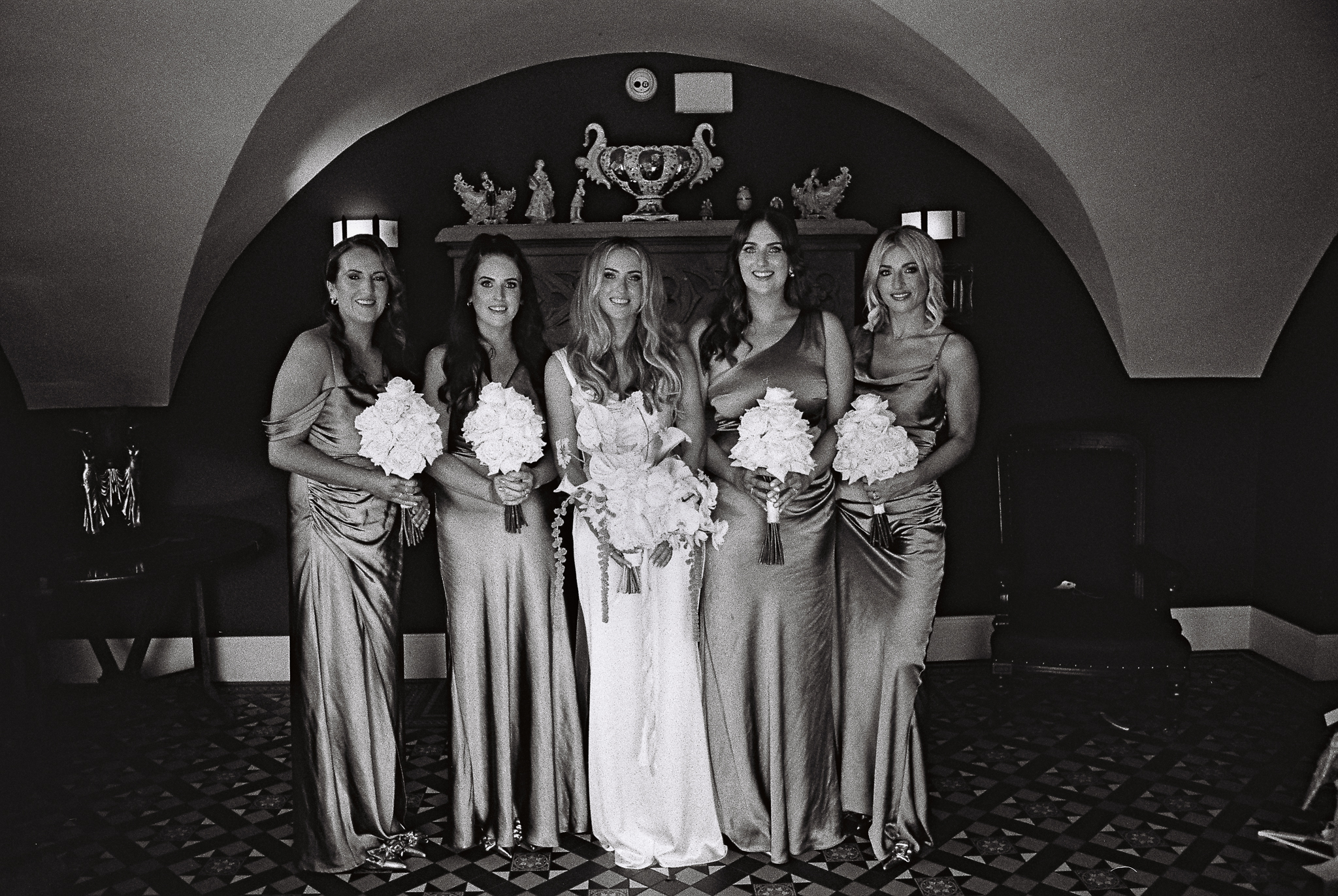 Black and white 35mm film group portrait of a bride and her bridesmaids standing together beneath the arched ceiling of the Butler's Kitchen at Markree Castle, Sligo.