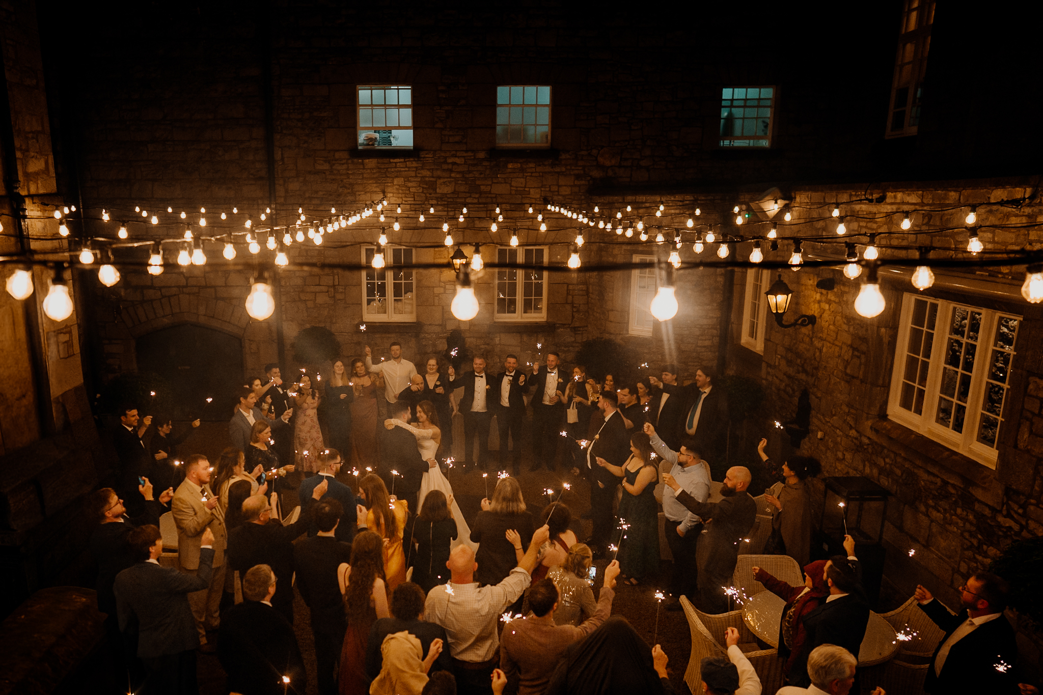 Romantic outdoor wedding first dance beneath festoon lights in the courtyard at Markree Castle after a rainy day.