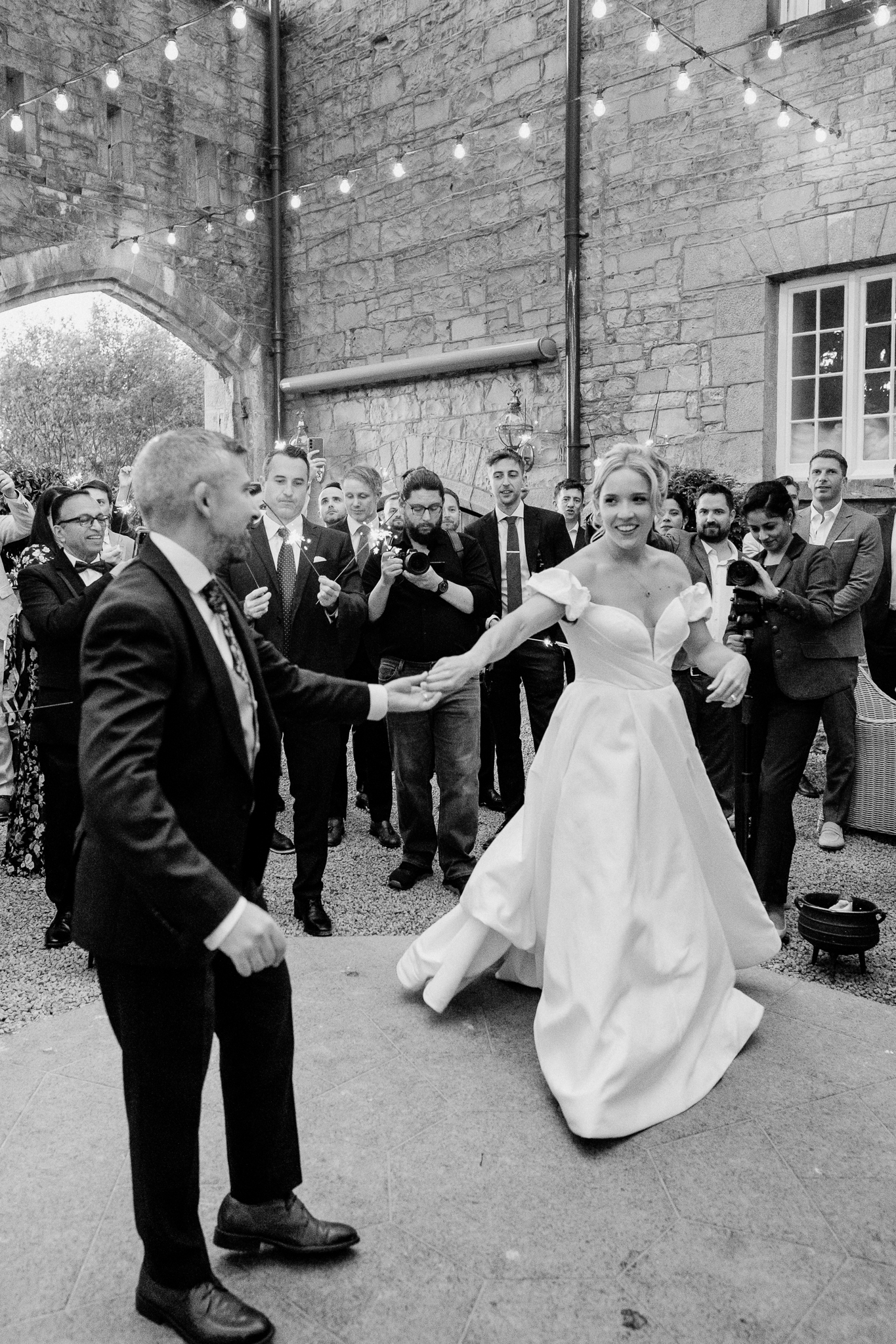 Black and white photograph of bride and groom dancing in front of applauding guests in the Markree Castle courtyard.