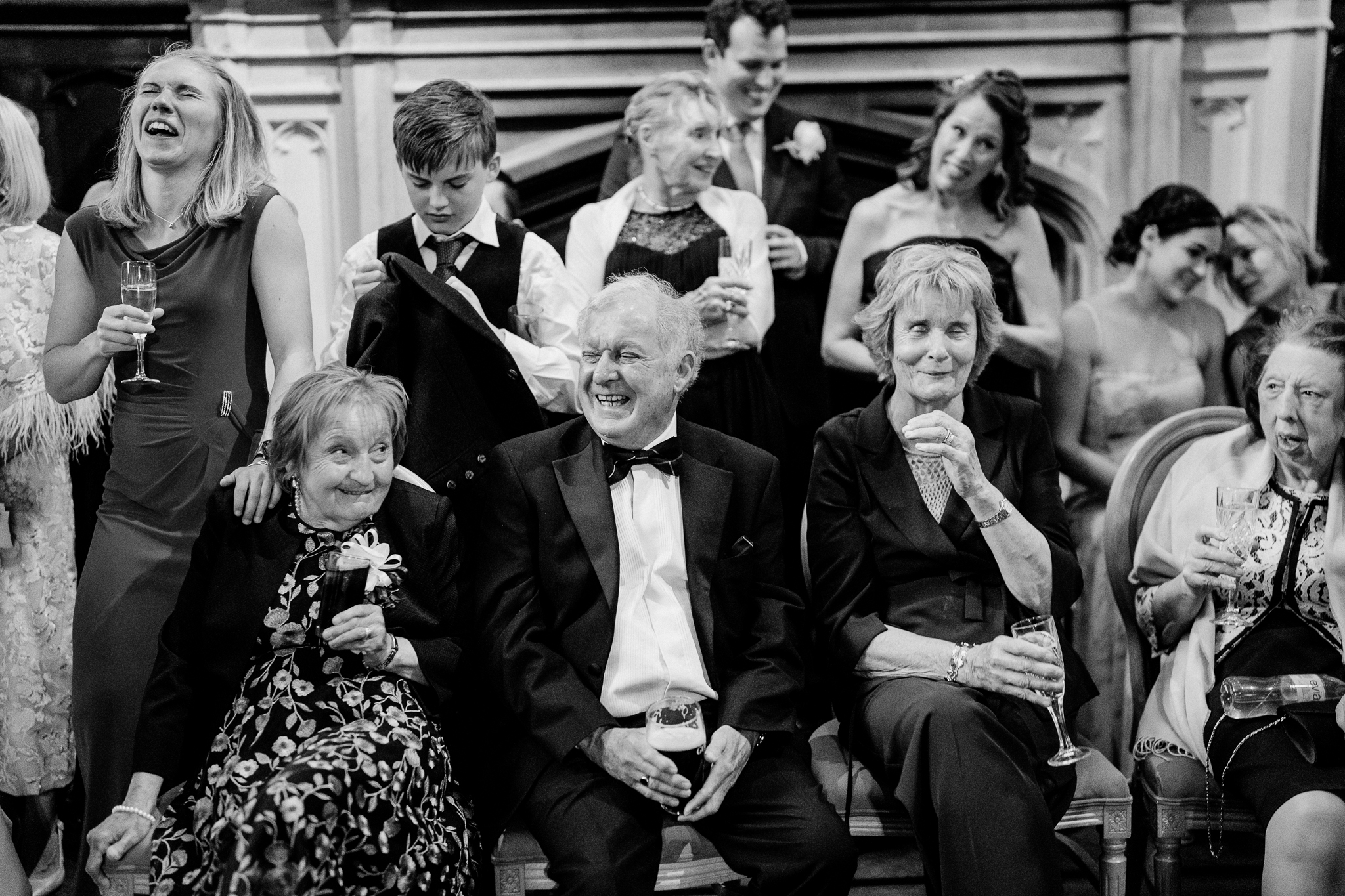 Black and white photograph of wedding guests smiling and reacting during speeches on the grand staircase at Markree Castle.