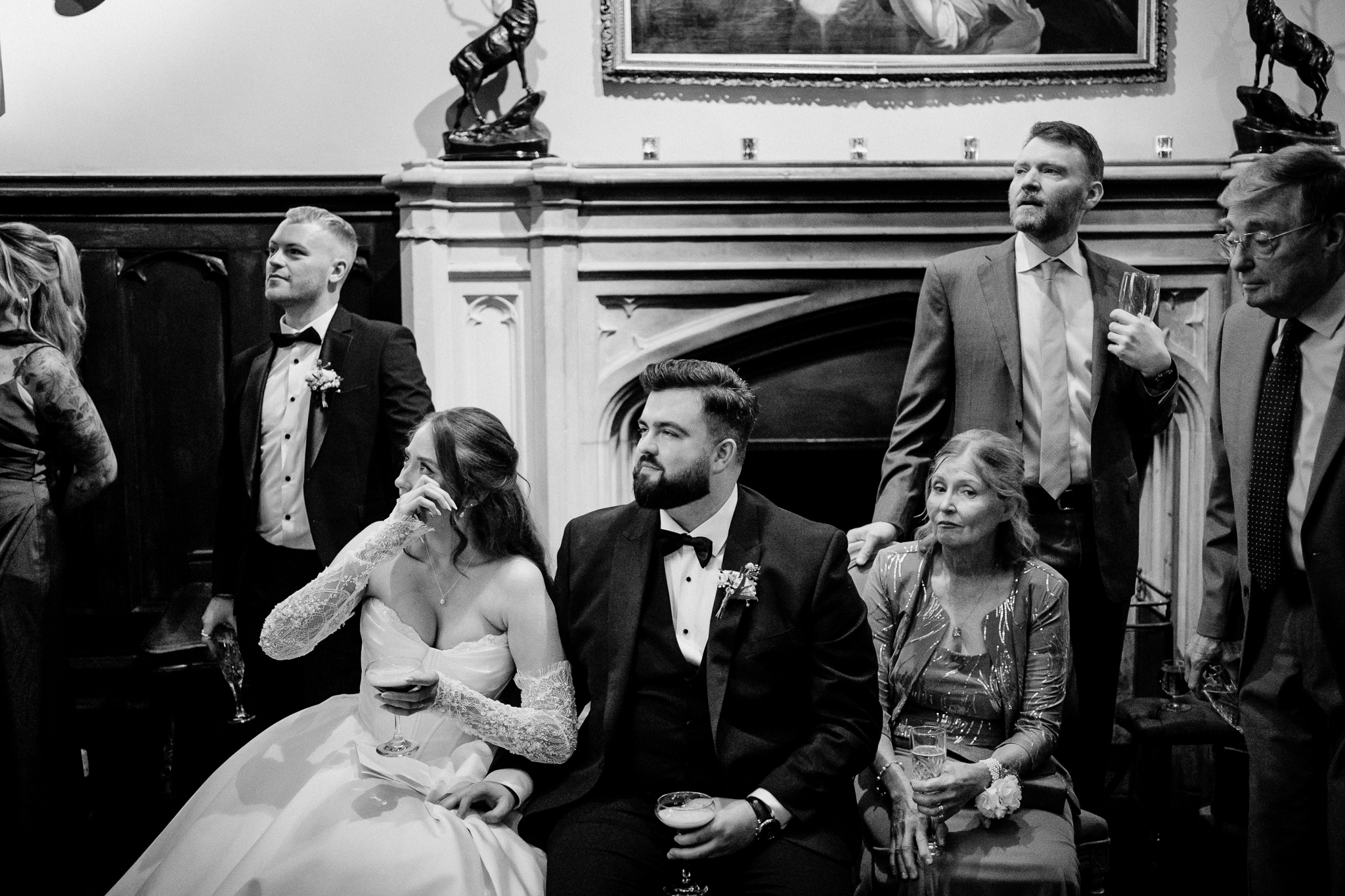 Black and white photograph of wedding guests laughing during speeches beside the ornate fireplace at Markree Castle.